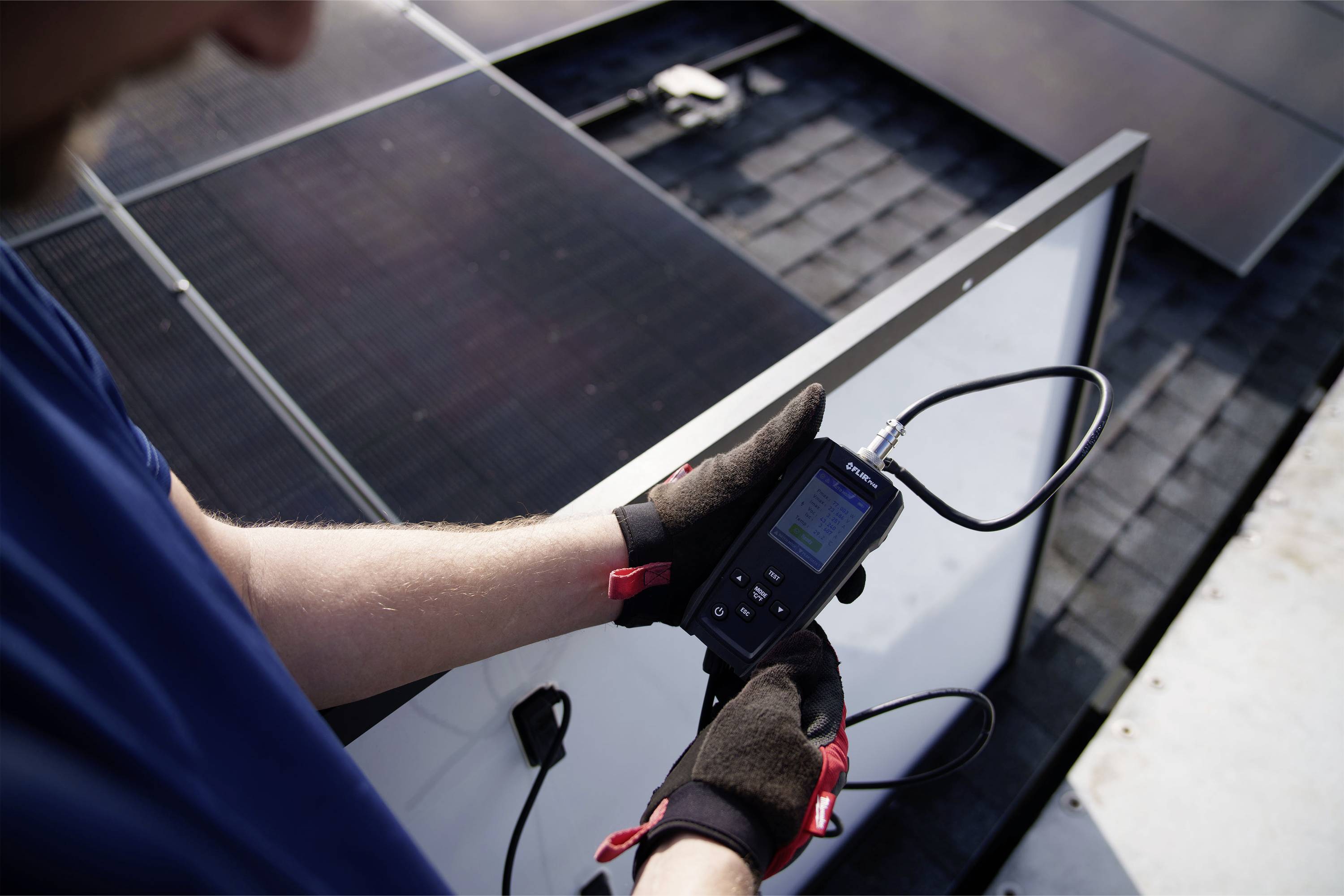 Een persoon meet de prestaties van zonnepanelen op een dak met een elektronisch apparaat.