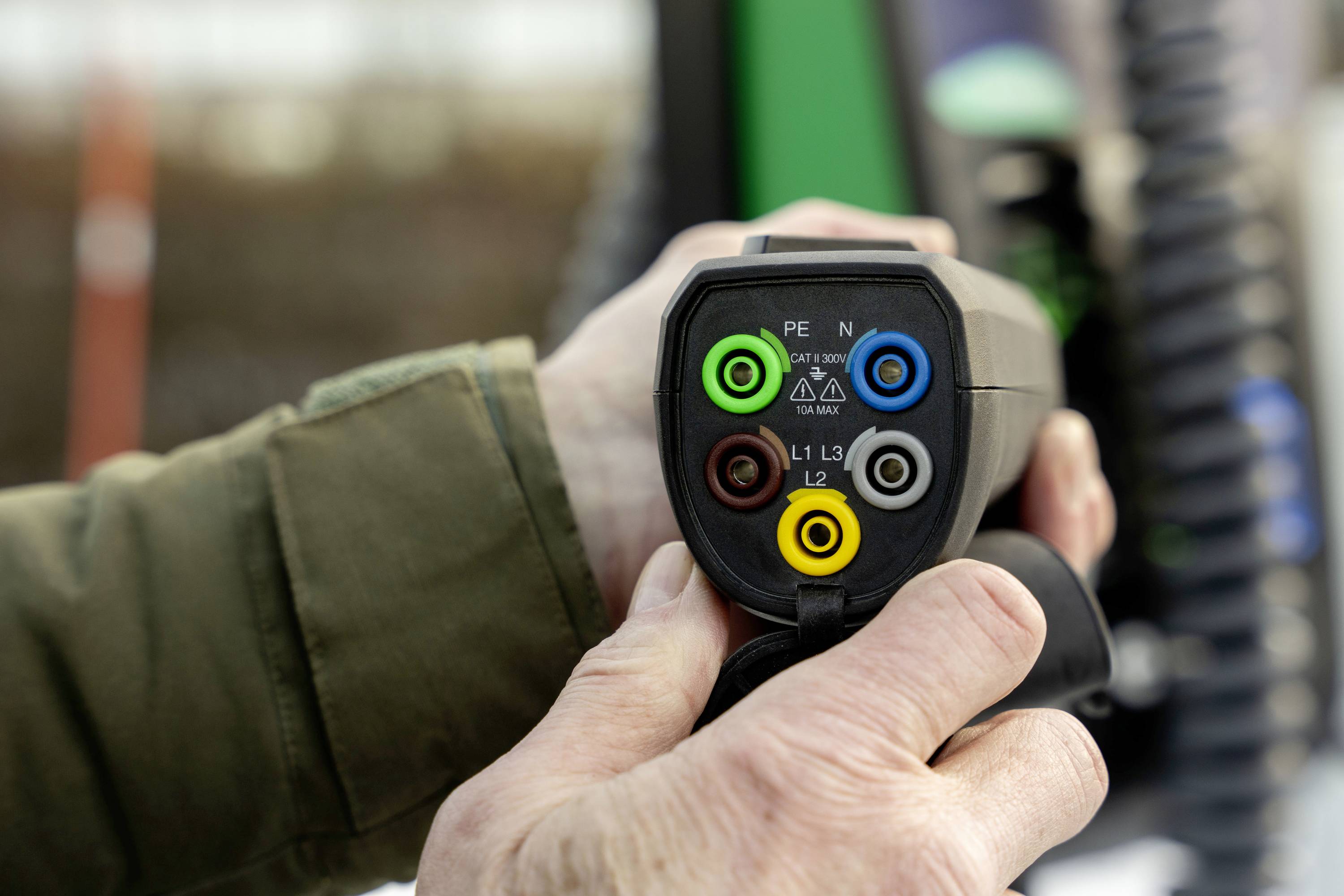 'Een persoon houdt een stekker vast met gekleurde aansluitcontacten: groen, blauw, bruin, geel, zwart. Mogelijk voor elektrische voertuigen.'