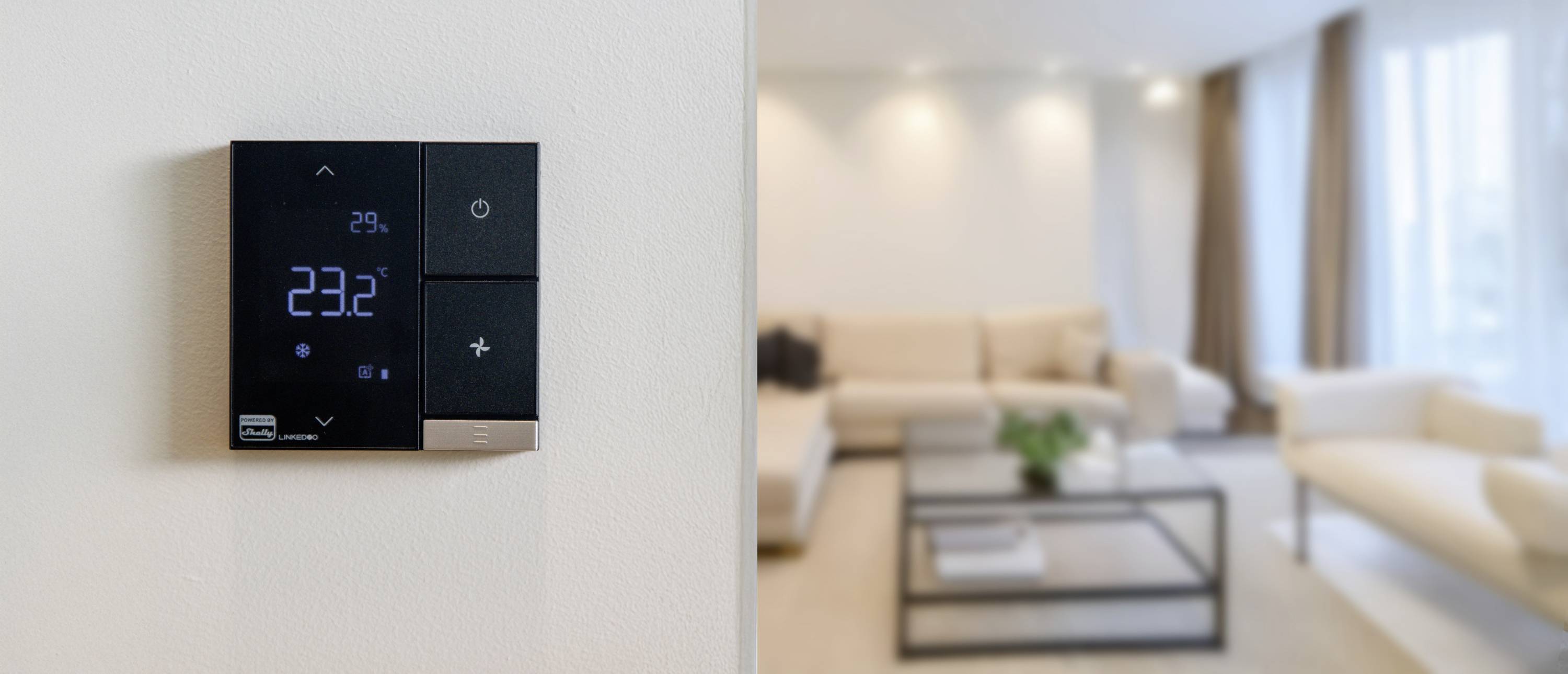 'Ruimtethermostaat aan de muur toont 23,2°C. Achtergrond: moderne woonkamer met lichte meubels.'