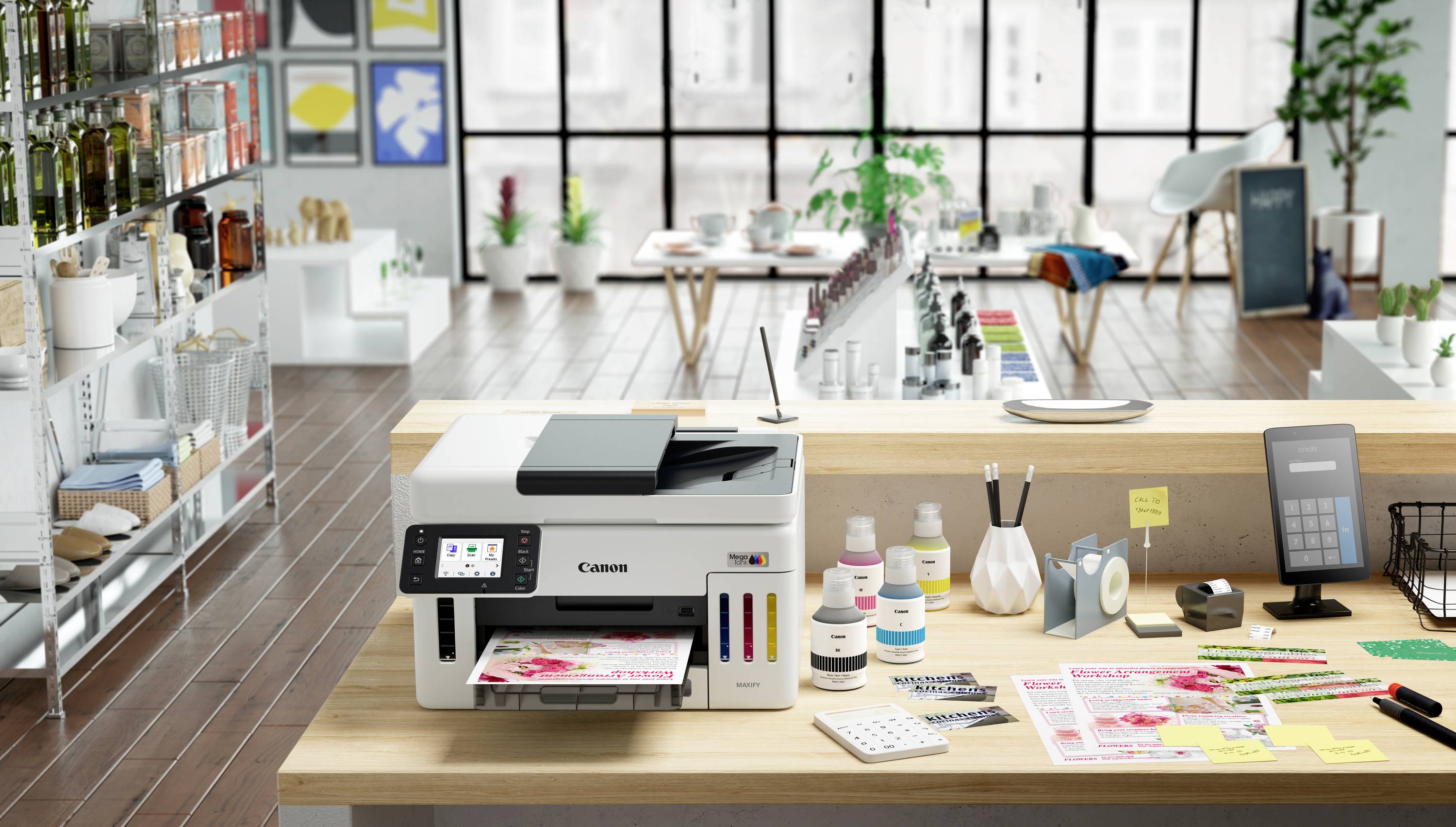 Een moderne printer op een houten bureau in een lichte kantoorruimte met planten en kantoorbenodigdheden, prints en inktflesjes ernaast.