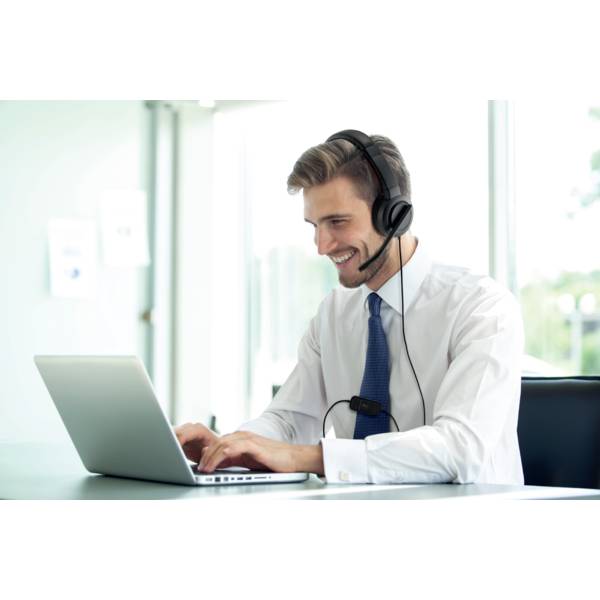 Een lachende man draagt een headset en werkt op een laptop in een modern kantoor. Op de achtergrond zijn ramen zichtbaar.