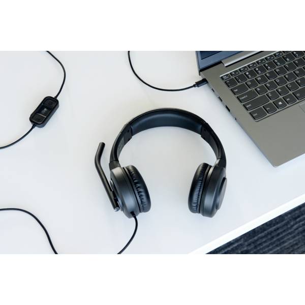 Koptelefoon met microfoon op een witte tafel naast een laptop. Illustreert een kantoor- of thuiswerkplek voor communicatie.