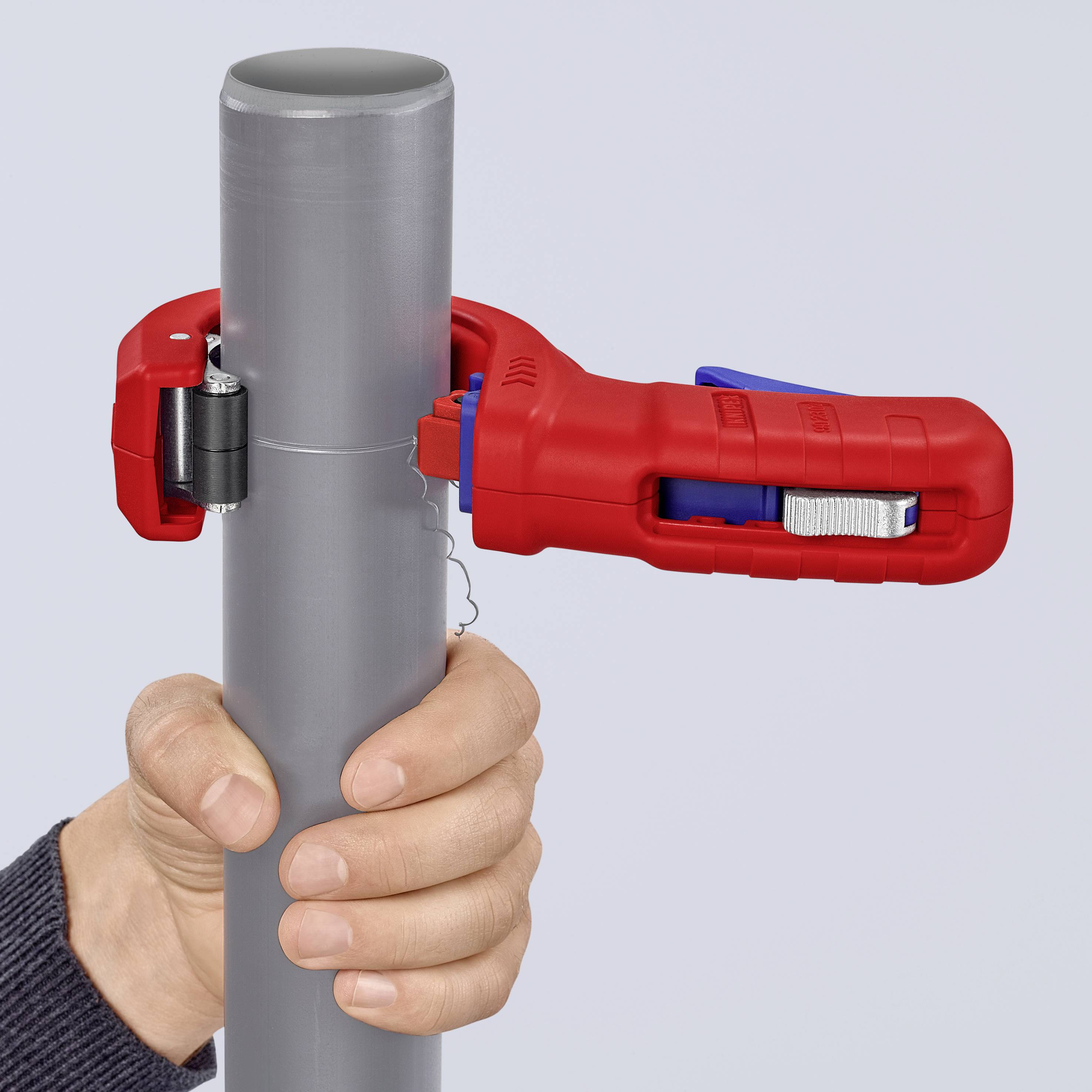 Een hand houdt een grijze pijp vast met een rode buissnijder. De buissnijder is om de pijp bevestigd en klaar om te snijden.