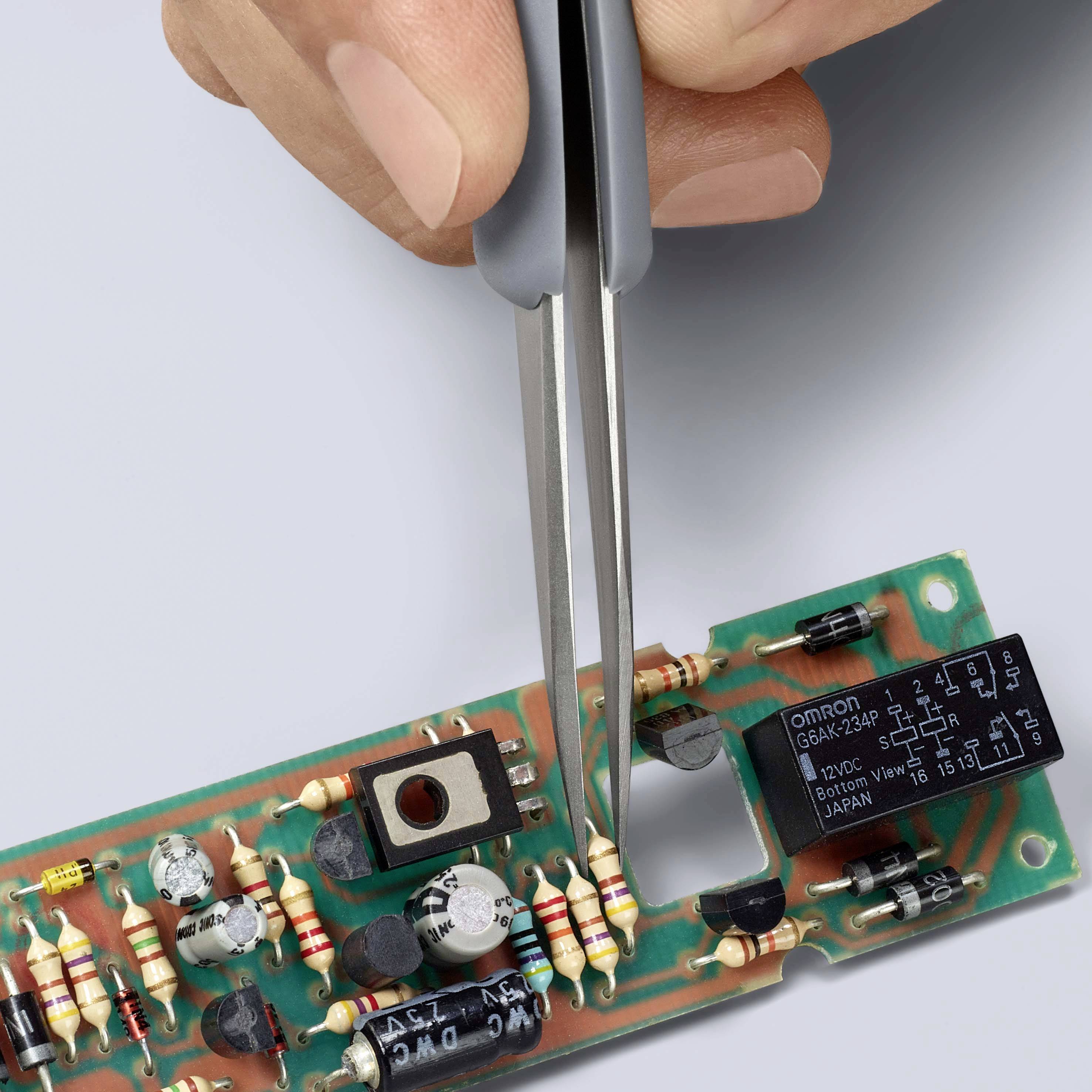 Een hand houdt een tang vast om een weerstand te plaatsen op een printplaat. De printplaat is uitgerust met elektronische componenten.