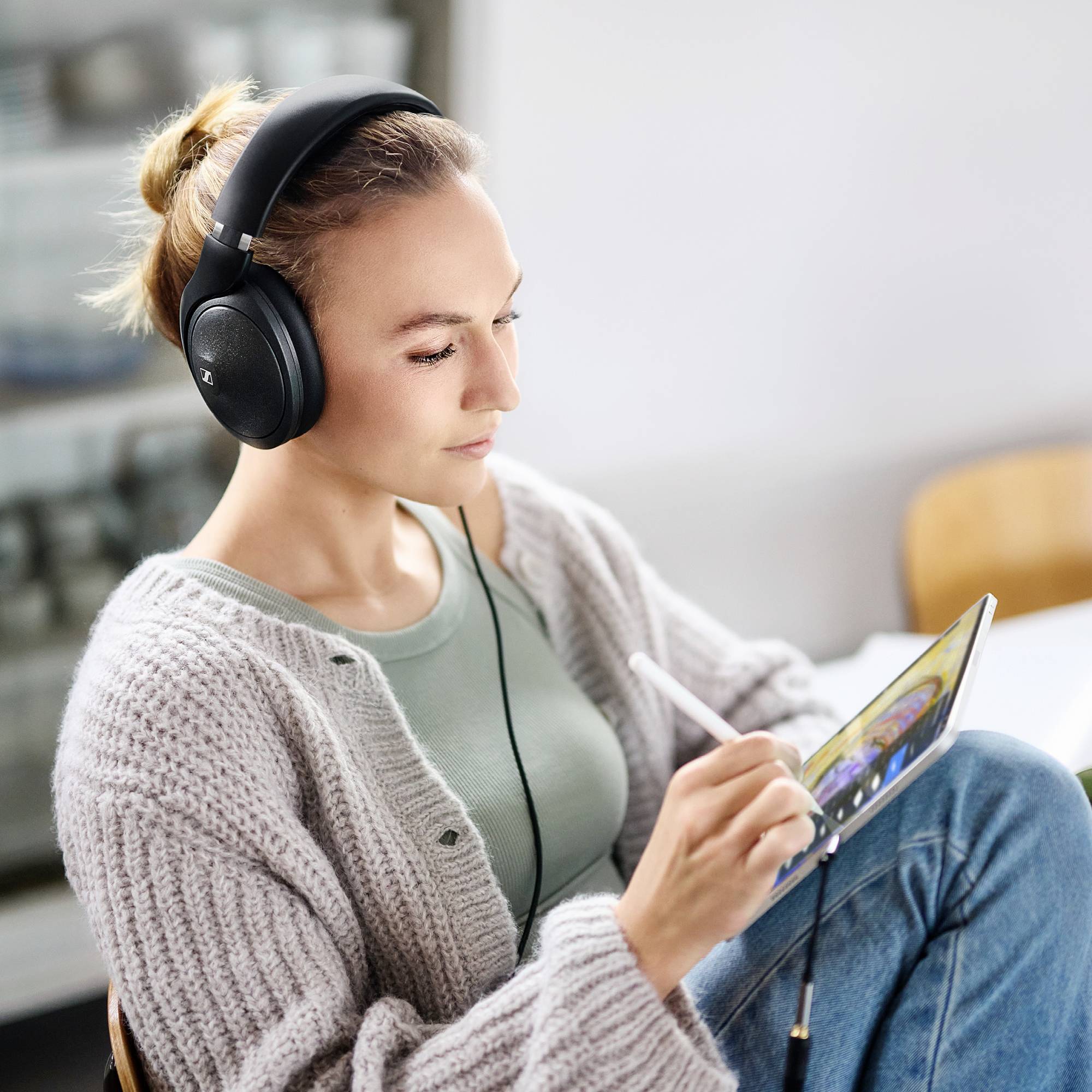 Vrouw draagt koptelefoon, concentreert zich op een tablet. Modern techniekgebruik in een ontspannen omgeving.