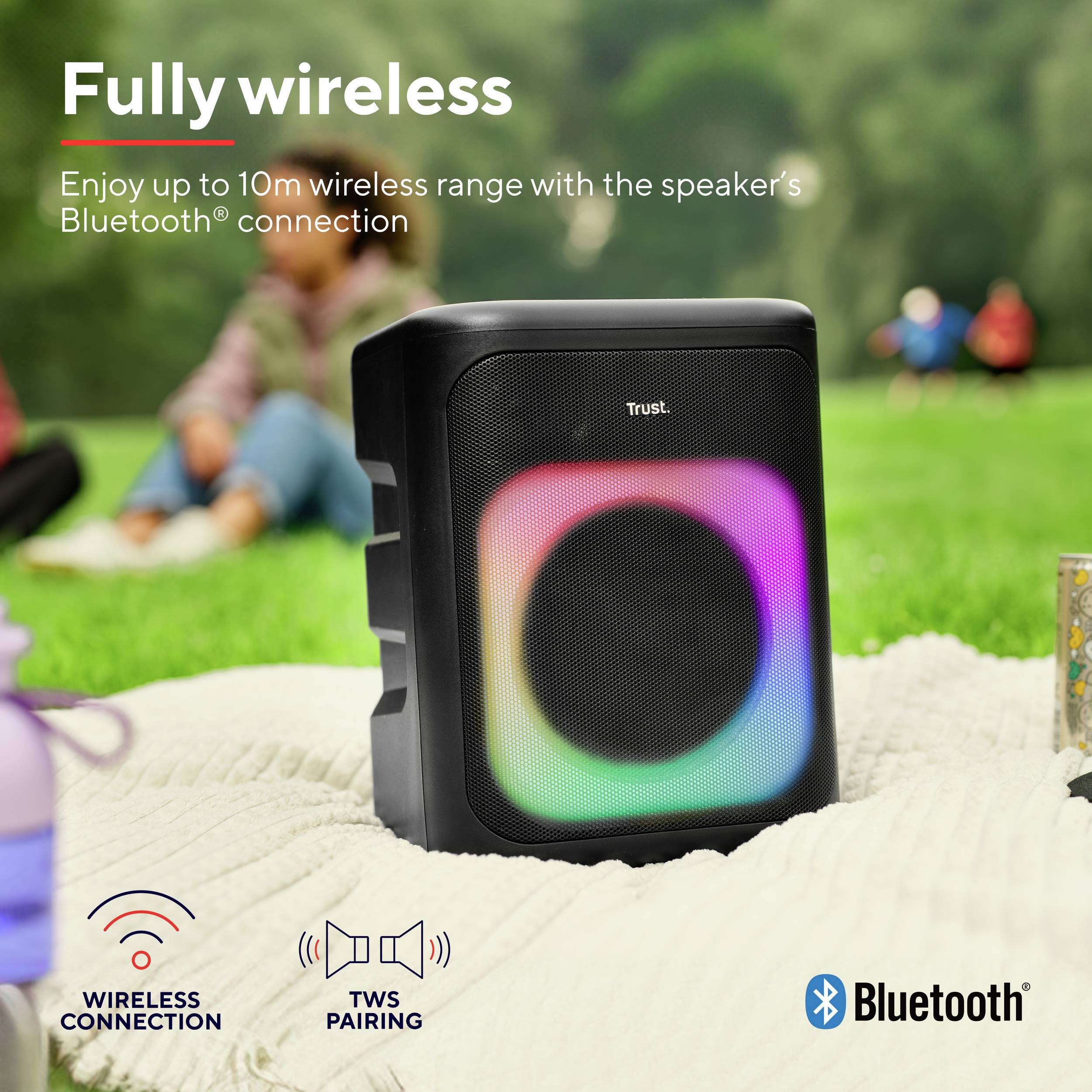 Draadloze WLAN-speaker op picknicklaken in het park. Tekst: 'Volledig draadloos'. Gekleurde verlichting op de speaker. Bluetooth- en verbindingssymbolen.