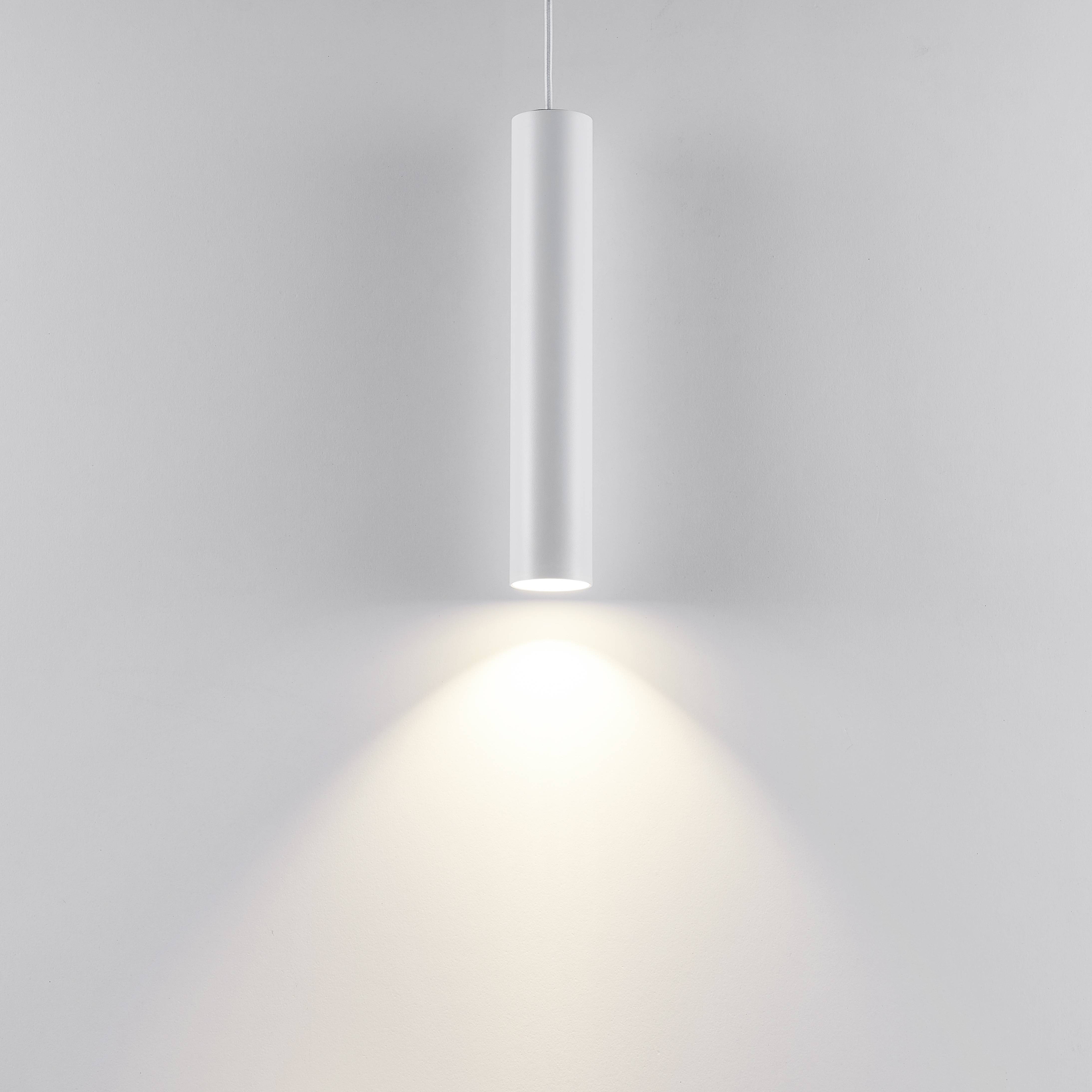 Een slanke, cilindrische hanglamp straalt zacht, warm licht naar beneden en creëert een gelijkmatige lichtverspreiding.