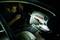 Een man doorzoekt 's nachts met een zaklamp het dashboardkastje van een auto. Het interieur is zwak verlicht.