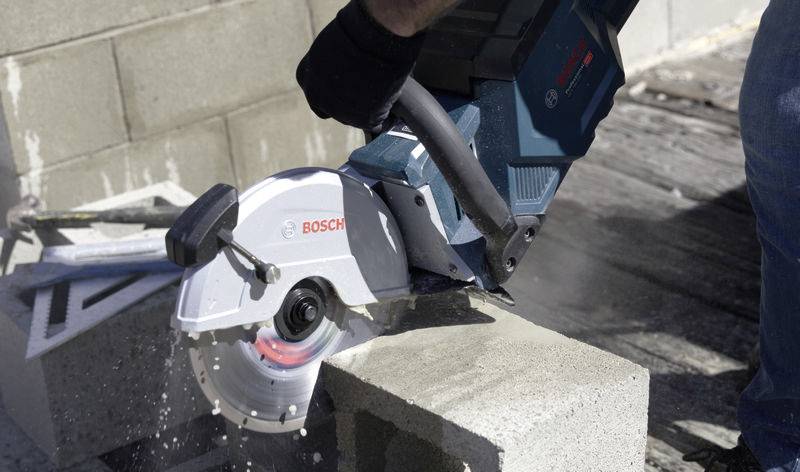 Een persoon zaagt een betonblok door met een Bosch-doorslijpmachine. Stof en puin vliegen rond tijdens het zagen.
