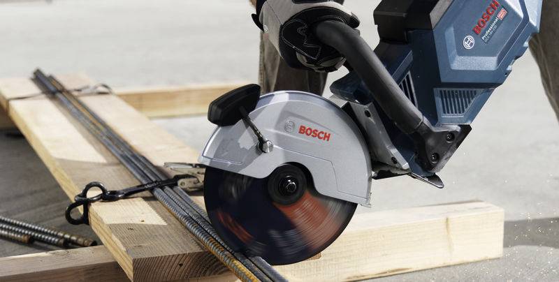 Een ambachtsman snijdt metalen staven door met een elektrische Bosch-doorslijpmachine op een bouwplaats.
