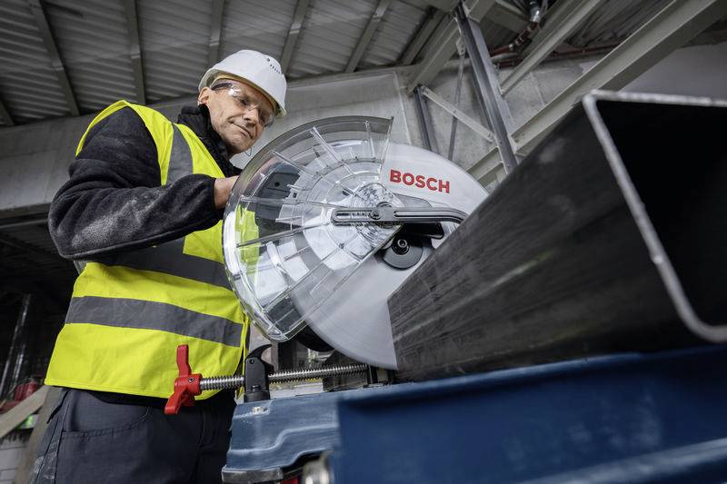 Een persoon in werkkleding en helm bedient een Bosch-zaag in een industriële omgeving.
