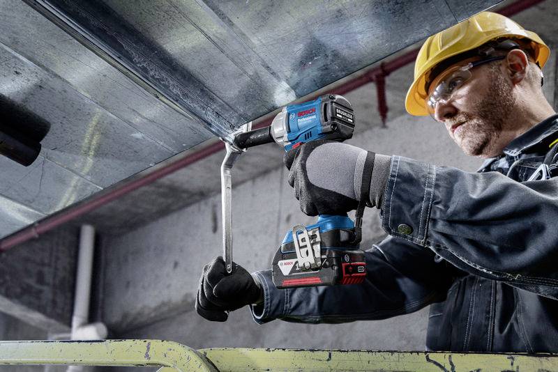 Een bouwvakker met veiligheidshelm schroeft met een accuschroevendraaier aan een metalen drager in een industriële omgeving.