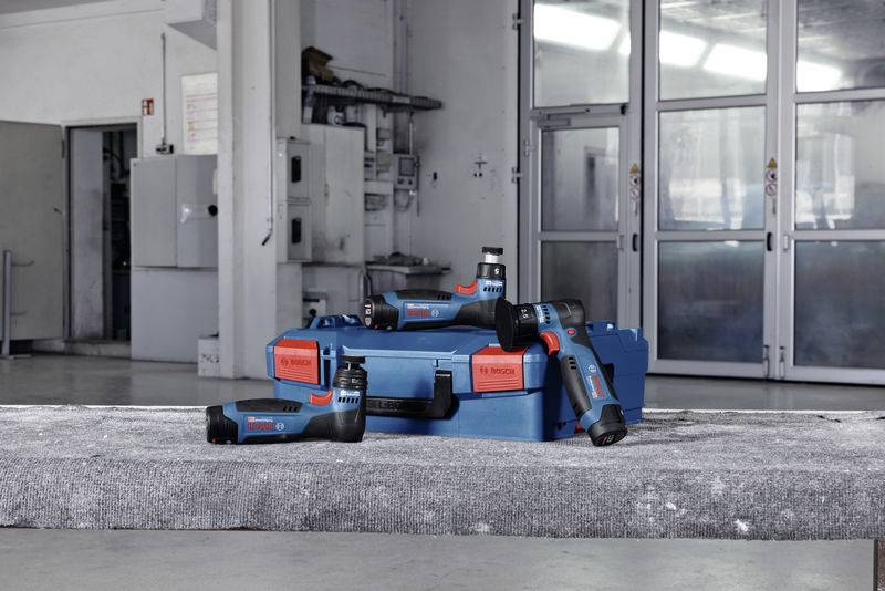 Accuschroevendraaier-set met blauwe en rode gereedschappen voor een grijze achtergrond in een werkplaats, duidelijk zichtbaar geplaatst op een tafel.