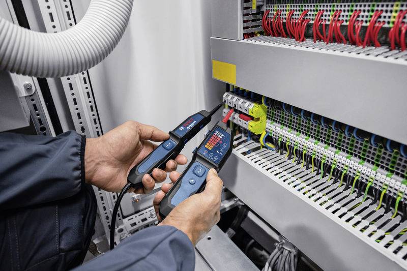 Een persoon test elektrische verbindingen in een schakelkast met een digitaal meetapparaat.