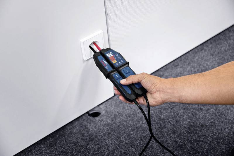 Een hand houdt een elektrisch testapparaat vast dat in een stopcontact wordt gestoken om de stroomtoevoer te controleren.