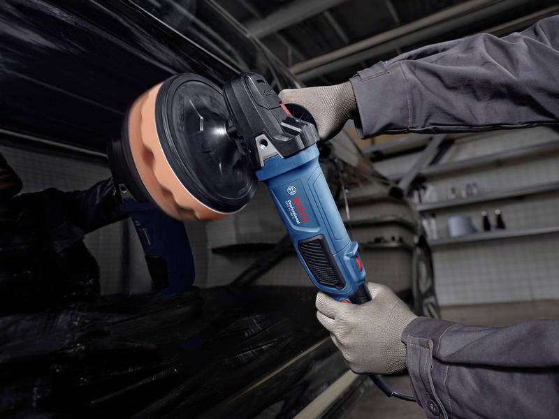 Een persoon polijst een auto met een elektrische polijstmachine. De machine heeft een oranje polijstopzetstuk.