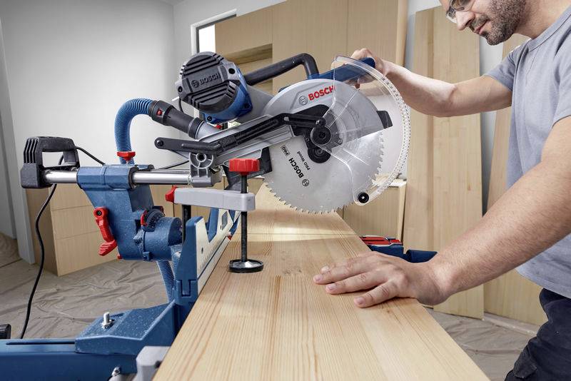 Een persoon zaagt een houten plank met een tafelcirkelzaag. De werkplaats is goed verlicht. De focus ligt op precies zagen.