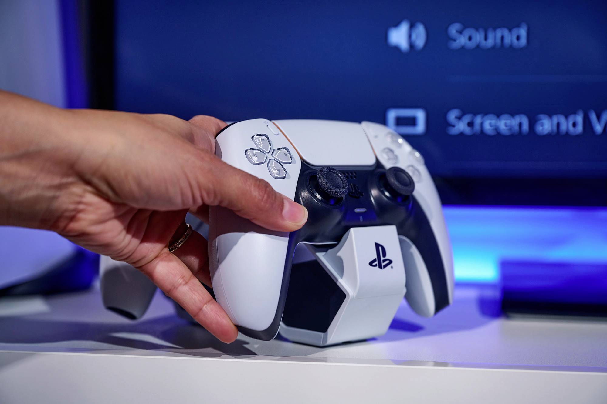Een hand houdt een witte gamingcontroller voor een scherm dat gebruikersinterfaceopties voor geluid en weergave toont.