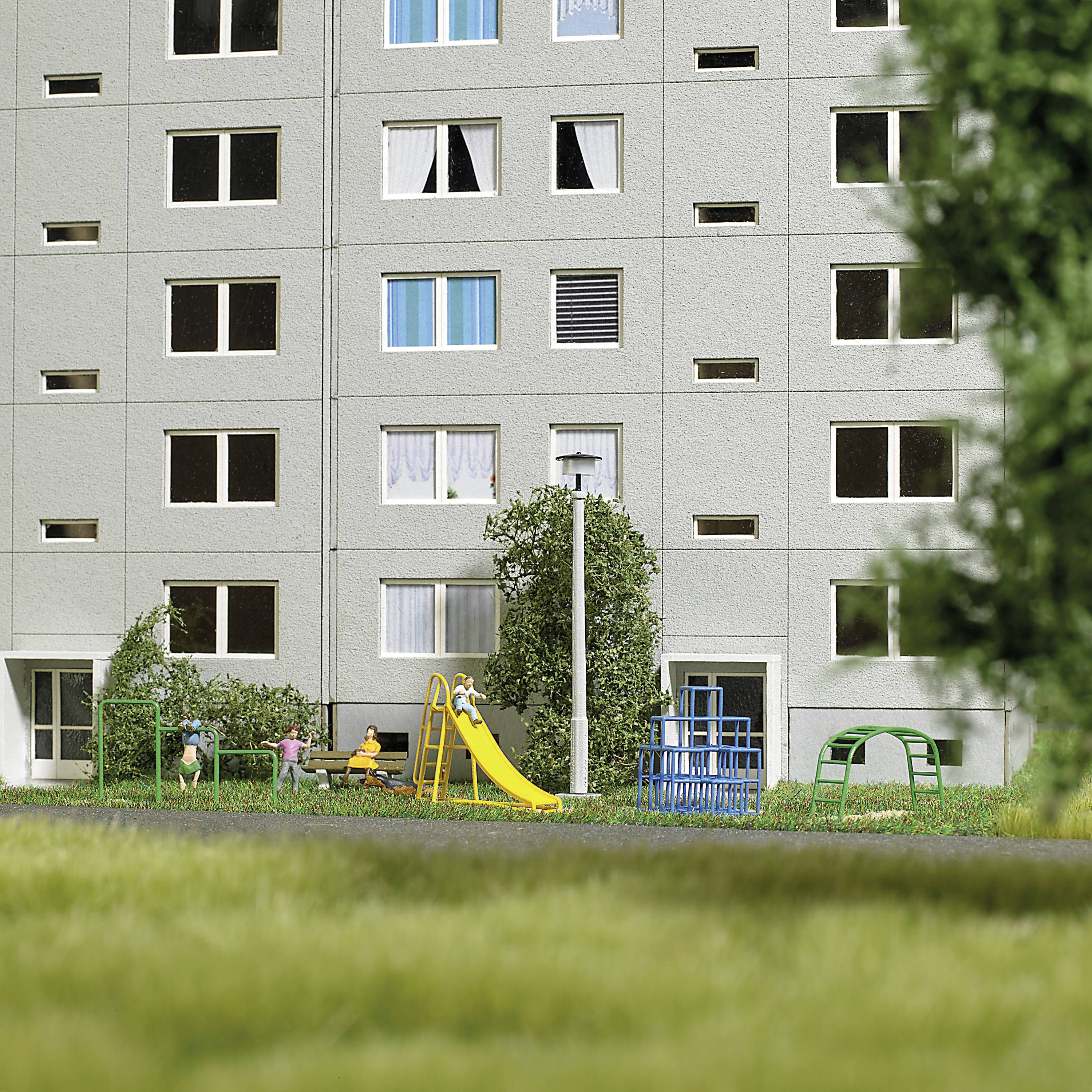 Woningblok met meerdere ramen, groene voorzieningen en een speelplaats op de voorgrond. Enkele mensen zijn te zien op de speelplaats.