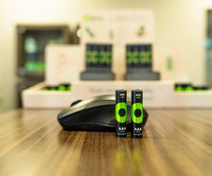 Twee groene AAA-batterijen staan op de voorgrond van een tafel, met een computermuis ernaast. Op de achtergrond zijn meer batterijen te zien in een display.
