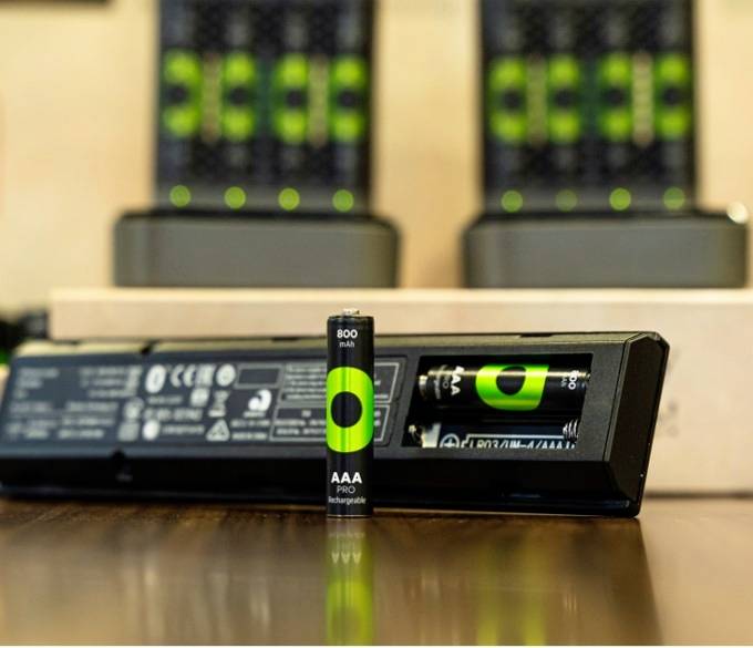 Een milieuvriendelijke AA-batterij van 800 mAh is in een oplader geplaatst. Op de achtergrond zijn verschillende vergelijkbare opladers zichtbaar.