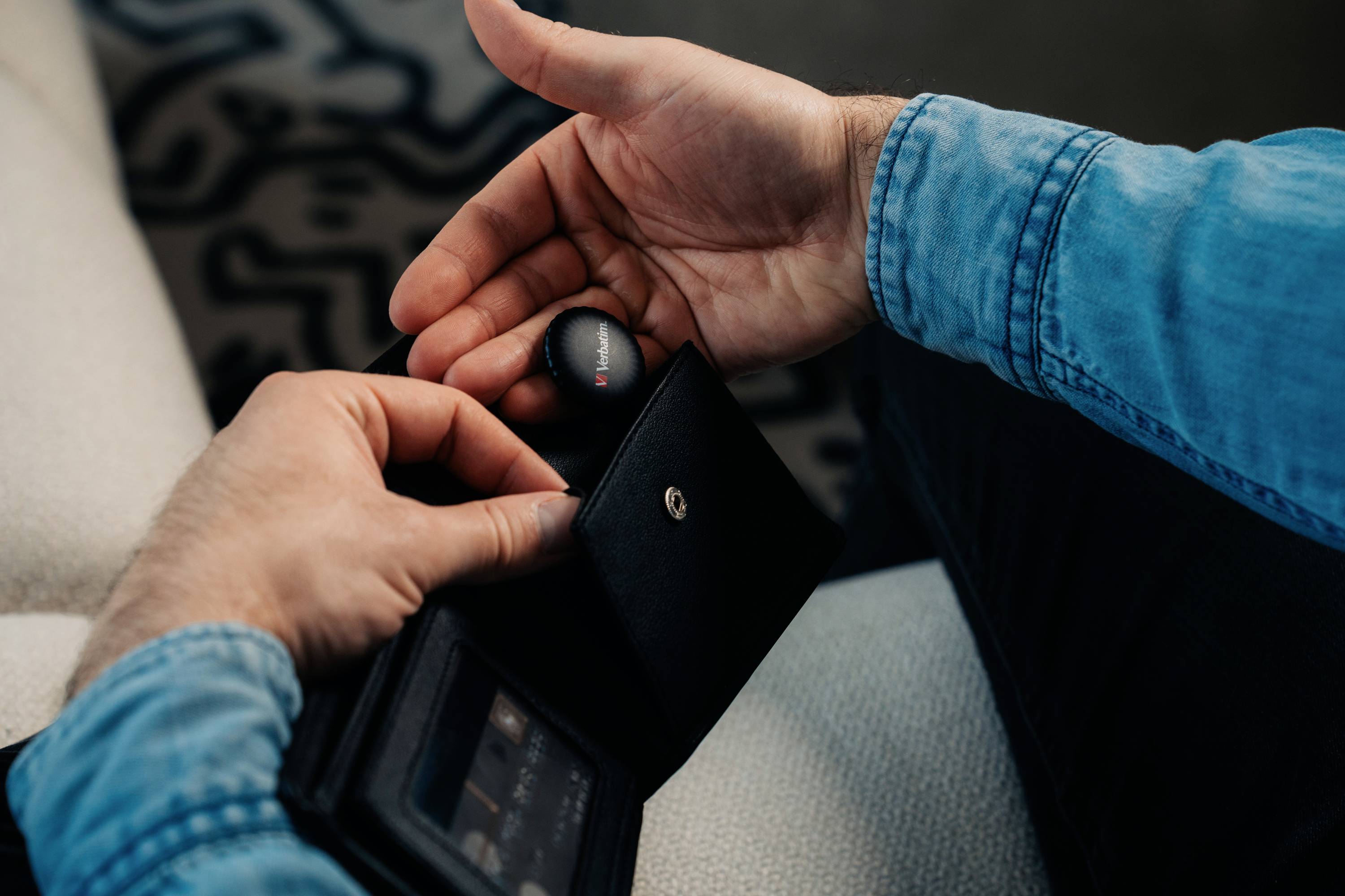 Een persoon in een spijkerblouse houdt een zwarte ronde lens vast en opent met zijn andere hand een zwart etui.