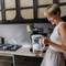 Vrouw in keuken giet water in glas. Moderne keuken met gaskookplaat op de achtergrond. Glimlachend en ontspannen.