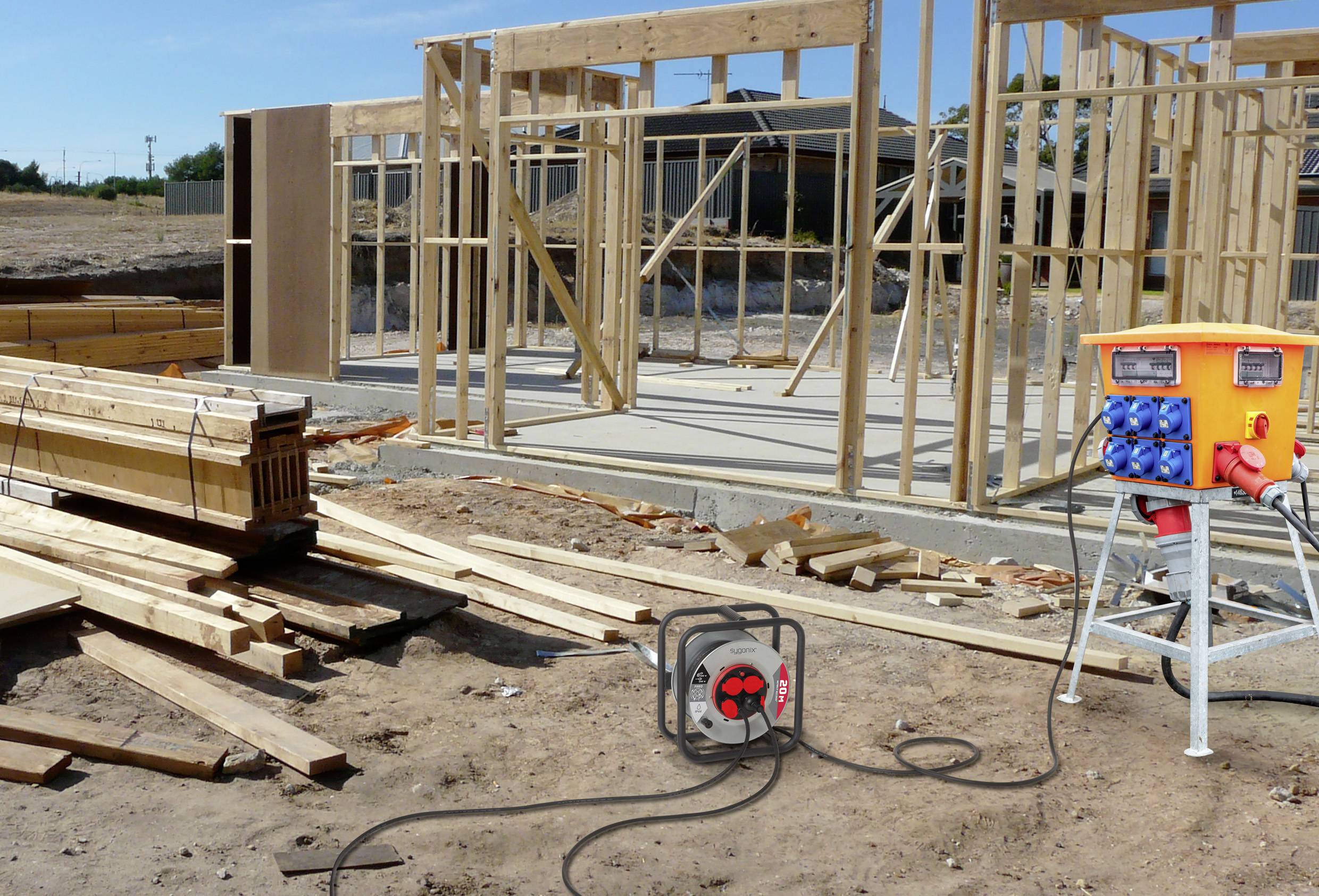 Houten raamwerk voor een nieuw huis in aanbouw, met elektrische apparatuur en hout verspreid op een zanderige locatie.