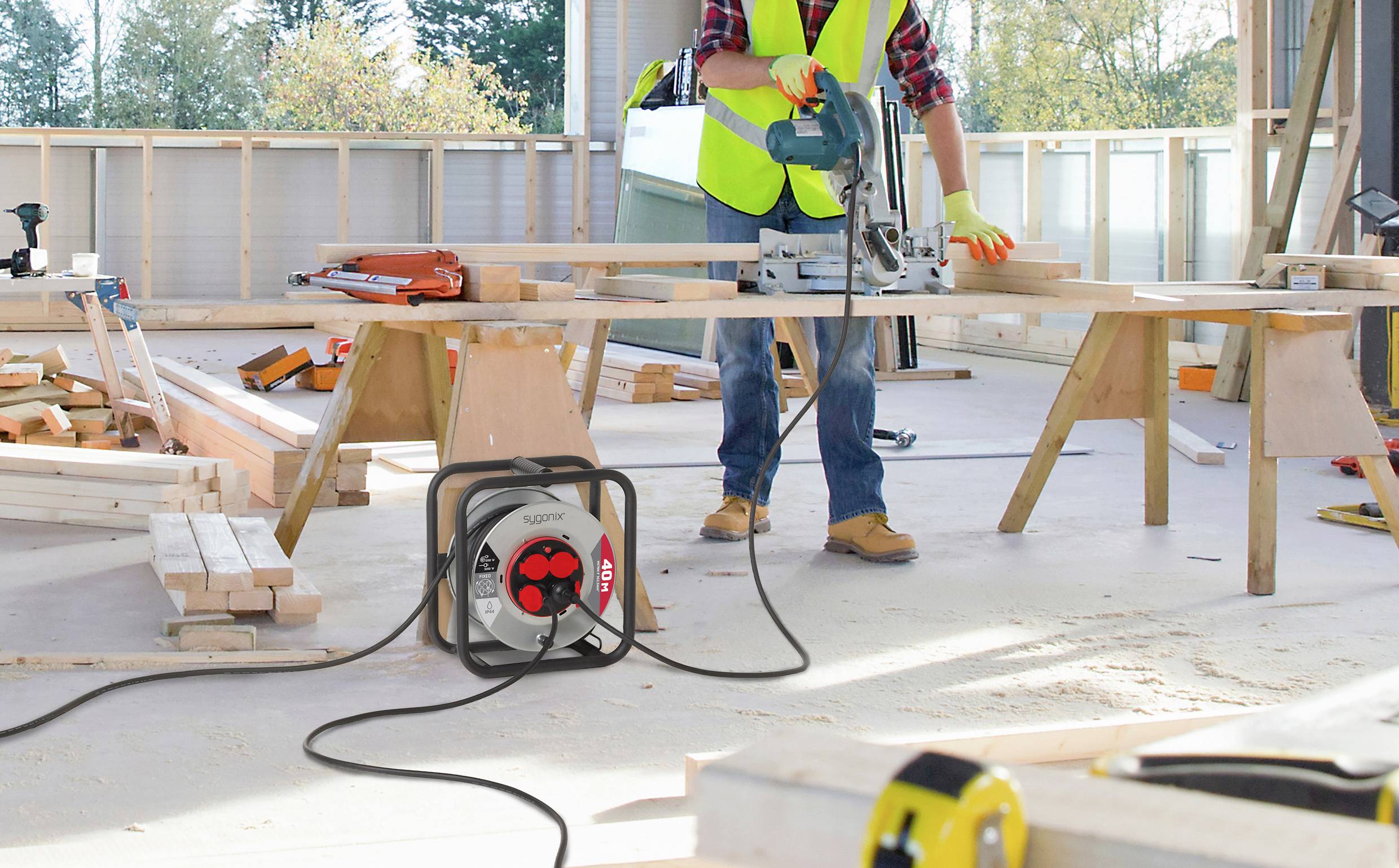 Een bouwvakker gebruikt een cirkelzaag op een houten plank in een lichte, onafgewerkte ruimte. Gereedschappen en houten balken zijn verspreid rond hem heen.