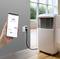 Een persoon houdt een smartphone vast waarop een thermostaat-app wordt weergegeven die een draagbare airconditioning bestuurt die is aangesloten op een slimme stopcontact.