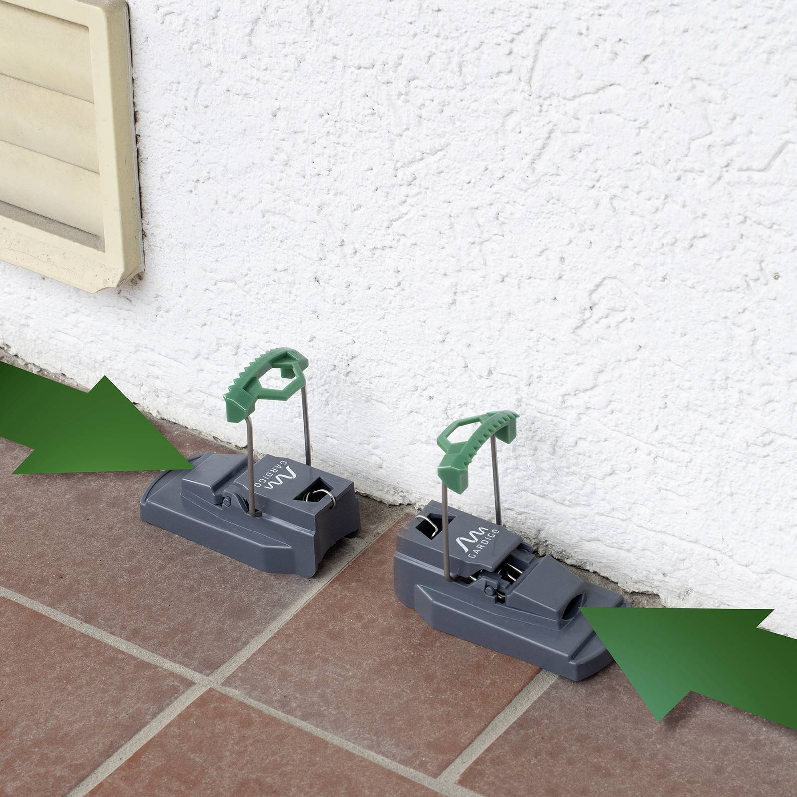 Twee grijze vallen met groene handgrepen aan een witte muur op terrastegels, klaargelegd voor ongedastebestrijding.