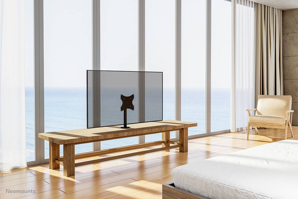 Een modern woonkamer met grote ramen en uitzicht op zee. Een televisie staat op een houten tafel, naast een fauteuil en een bed.