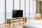 Een moderne ruimte met grote ramen toont een televisie op een houten tafel, met uitzicht op de zee. Naast de tv staat een fauteuil.