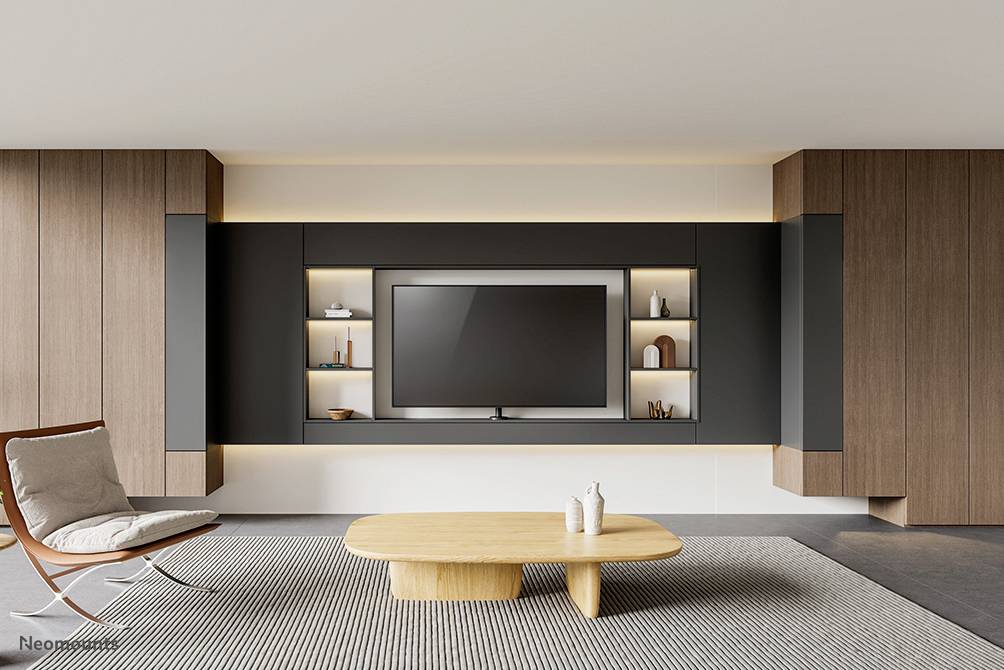 Modern woonkamer met houten accent. In het centrum een grote flatscreen-tv, omringd door planken en decoratie. Minimalistisch design.