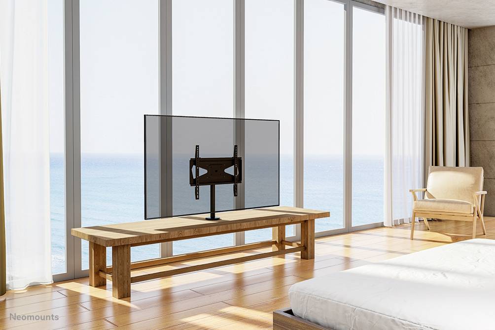 Een minimalistisch ingericht woonkamer met een groot raam en een televisie op een houten tafel. Uitzicht op de zee op de achtergrond.
