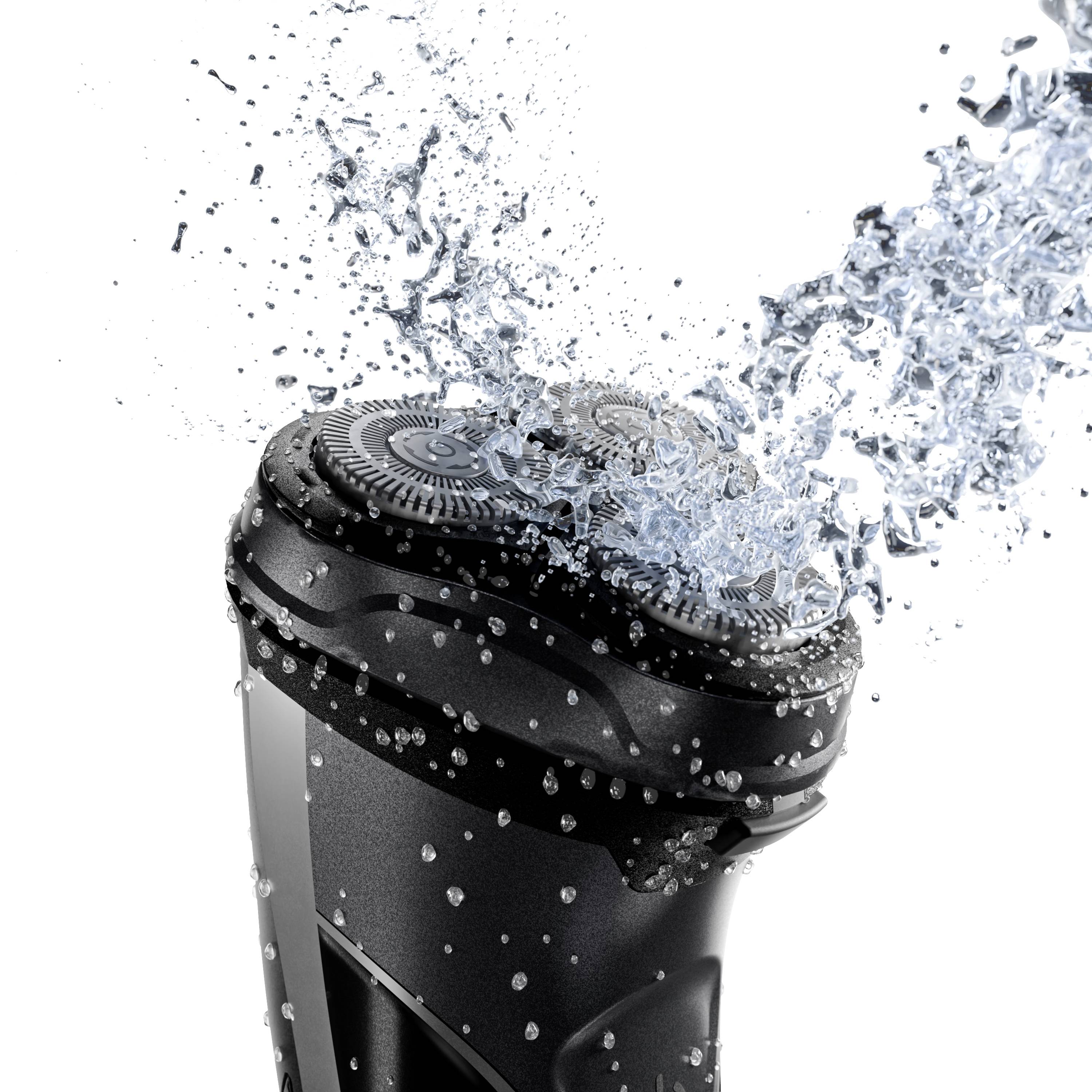 Een elektrische scheerapparaat dat zich onder stromend water bevindt voor reiniging. Waterdruppels spatten in de lucht.