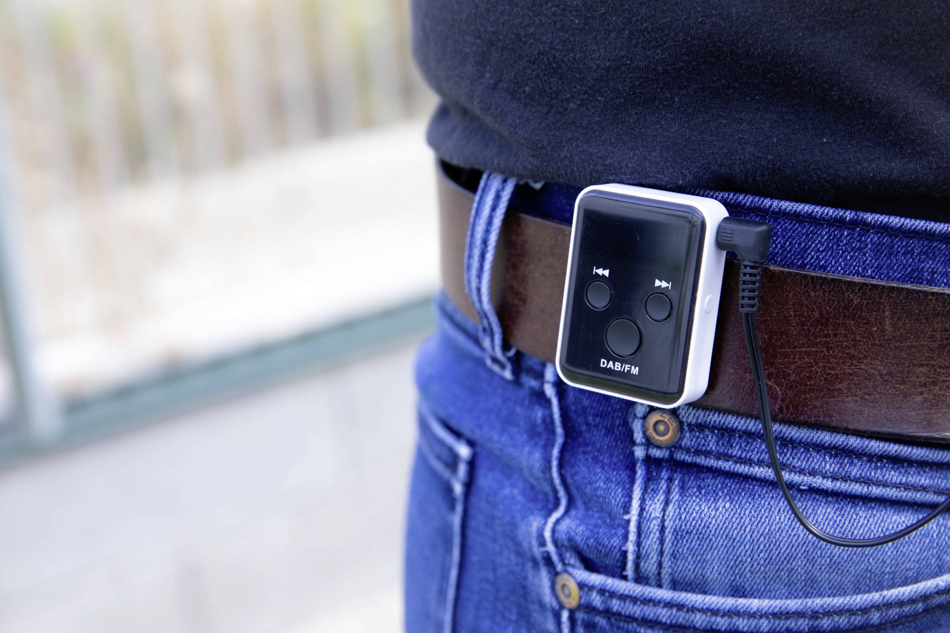 Een draagbare DAB-radio is bevestigd aan een bruine riem om de heupen van een persoon en toont bedieningsknoppen aan de voorkant.