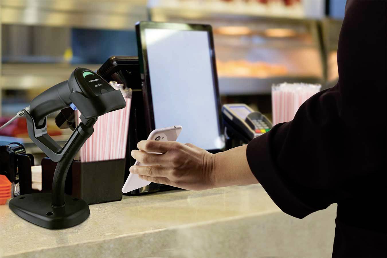 Een persoon houdt een smartphone bij een scanner op een balie, naast een kaartlezer, in een zakelijke omgeving.