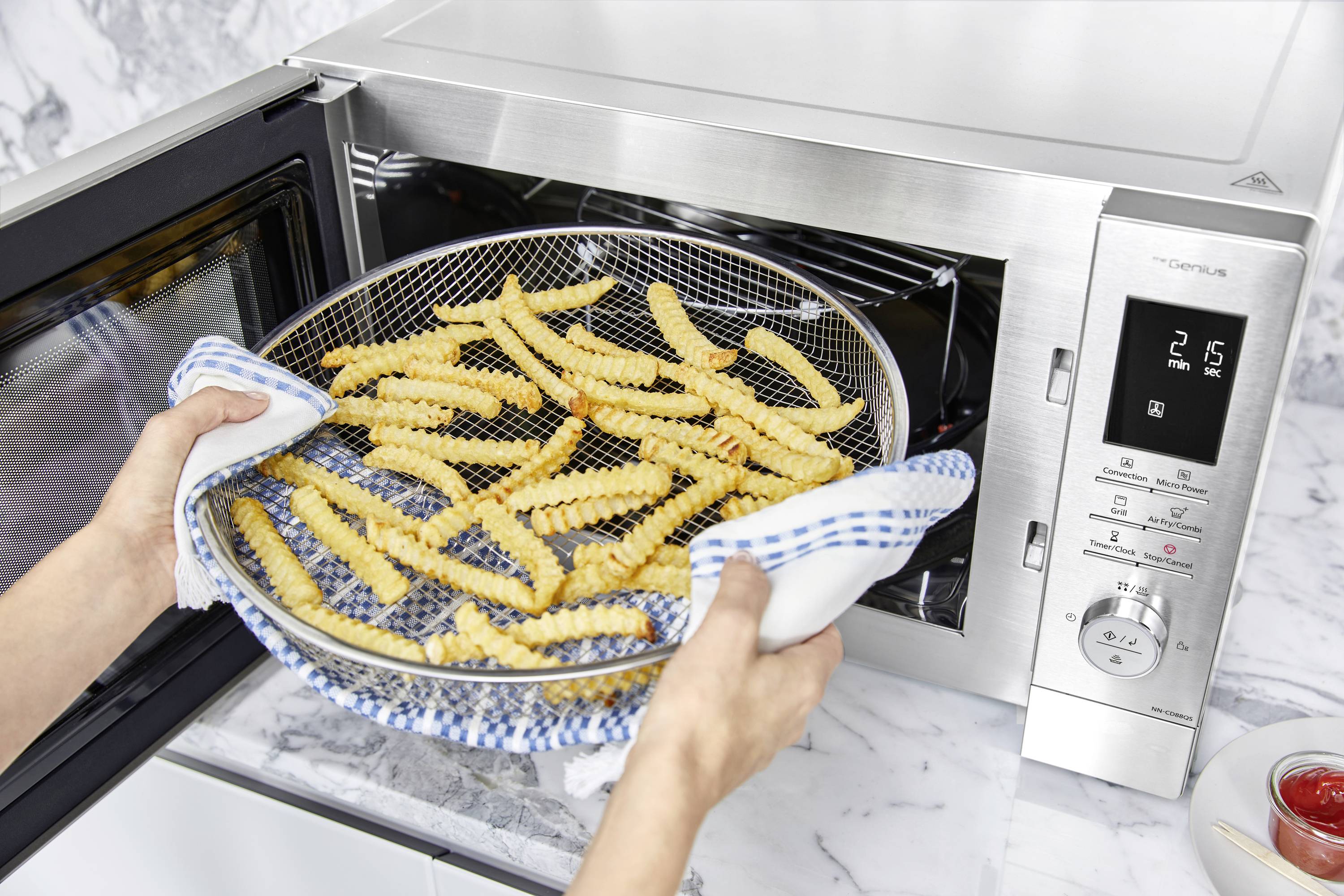 Een persoon haalt een dienblad met knapperige frietjes uit een magnetron. De magnetron toont de tijd.