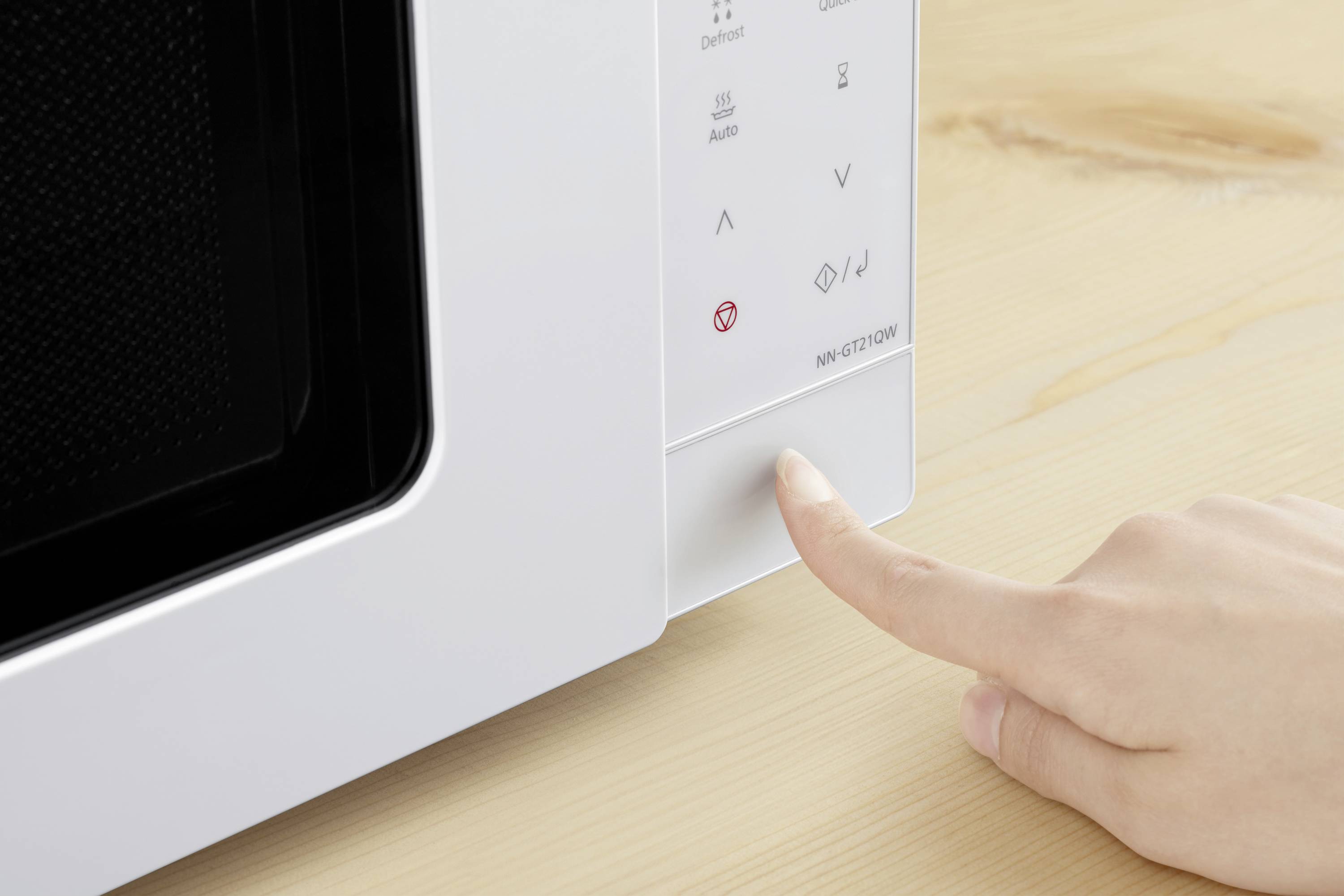 Een hand drukt op de starttoets van een witte magnetron op een houten tafel.