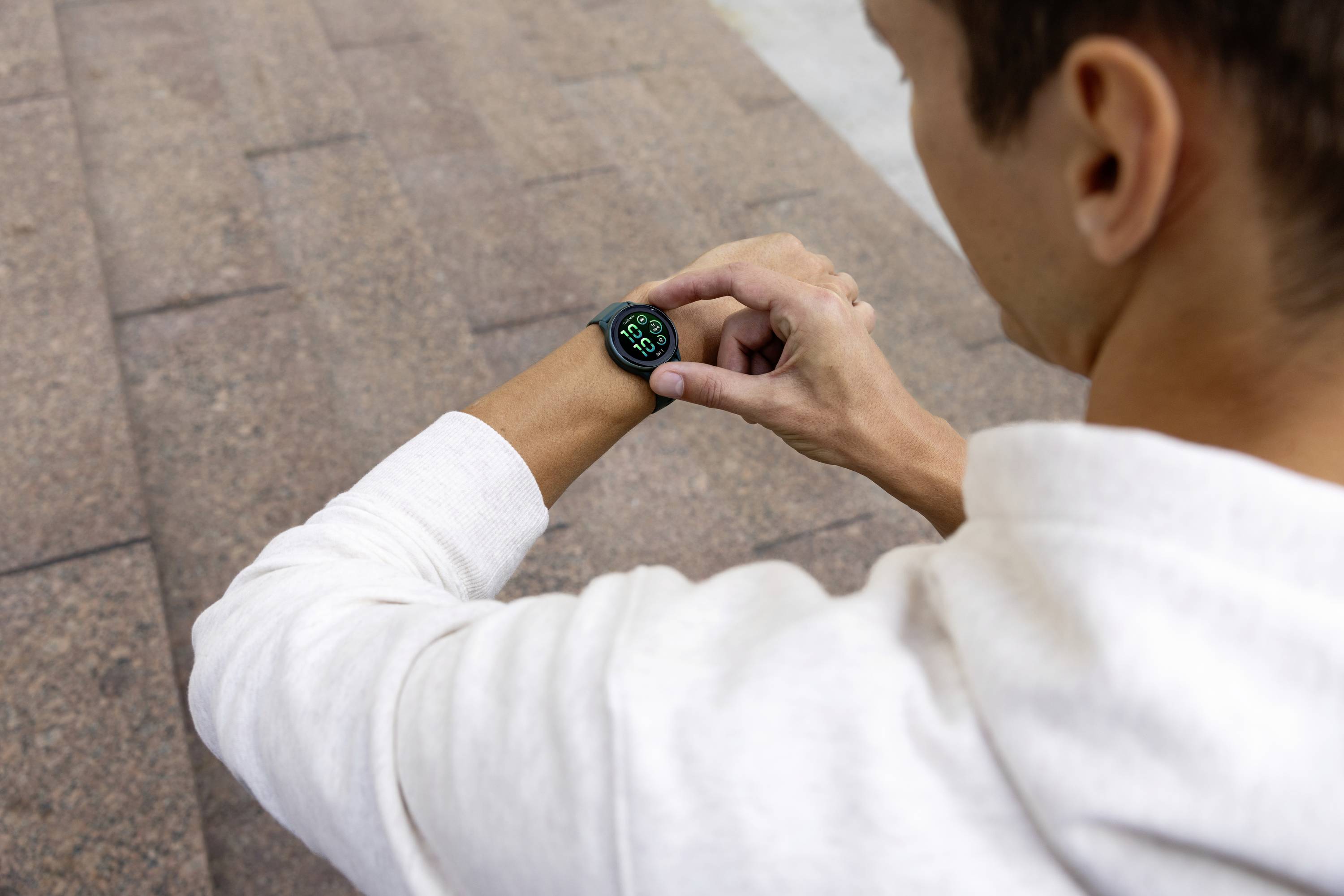 Een persoon tikt op een smartwatch terwijl hij/zij buiten op een stenen trap zit. Het horloge toont een groen display met symbolen.
