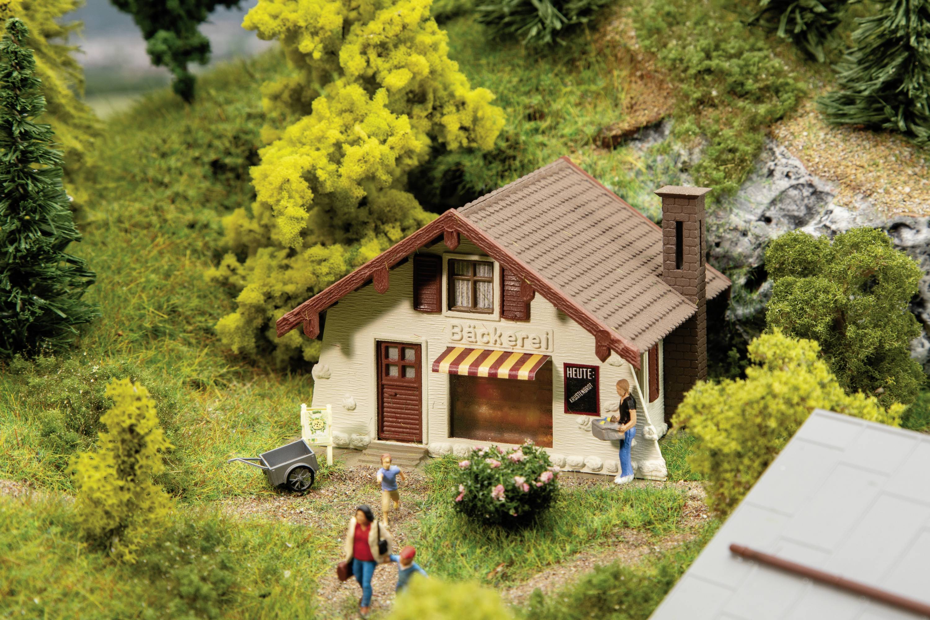 Een modelbakkerij in een landelijk miniatuurlandschap met figuren. Voor het huis staan een vrouw en een kind.