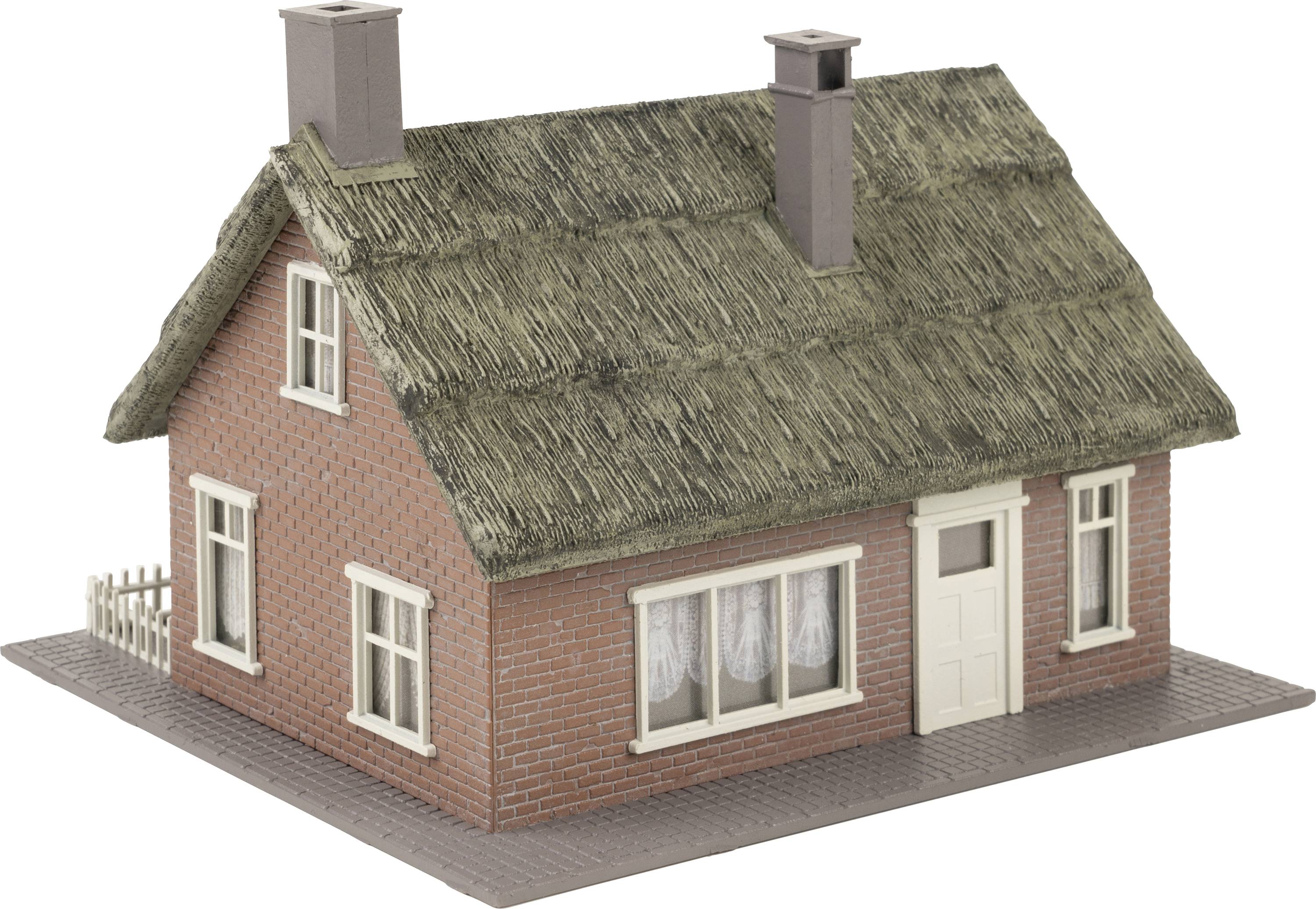 Een klein rood bakstenen huis met rieten dak, witte ramen en twee schoorstenen.