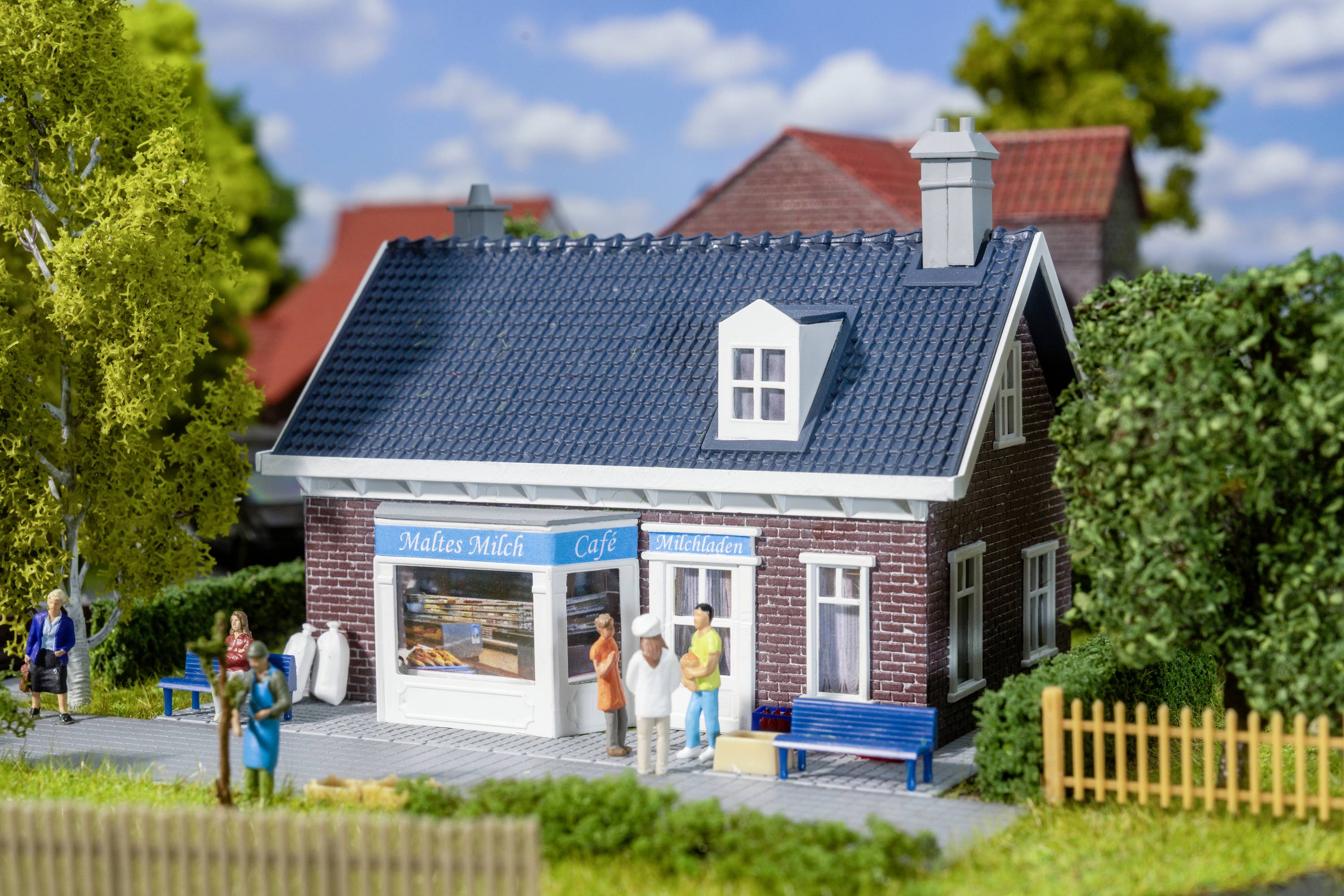 Een klein modelcafé met de tekst 'Maltes Melk Café', omringd door miniatuurbomen en figuurtjes die buiten staan.
