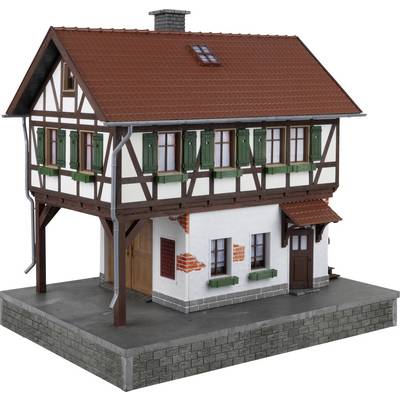 Een modelwoning in vakwerkstijl met een rood pannendak en groene luiken, geplaatst op een grijze sokkel.