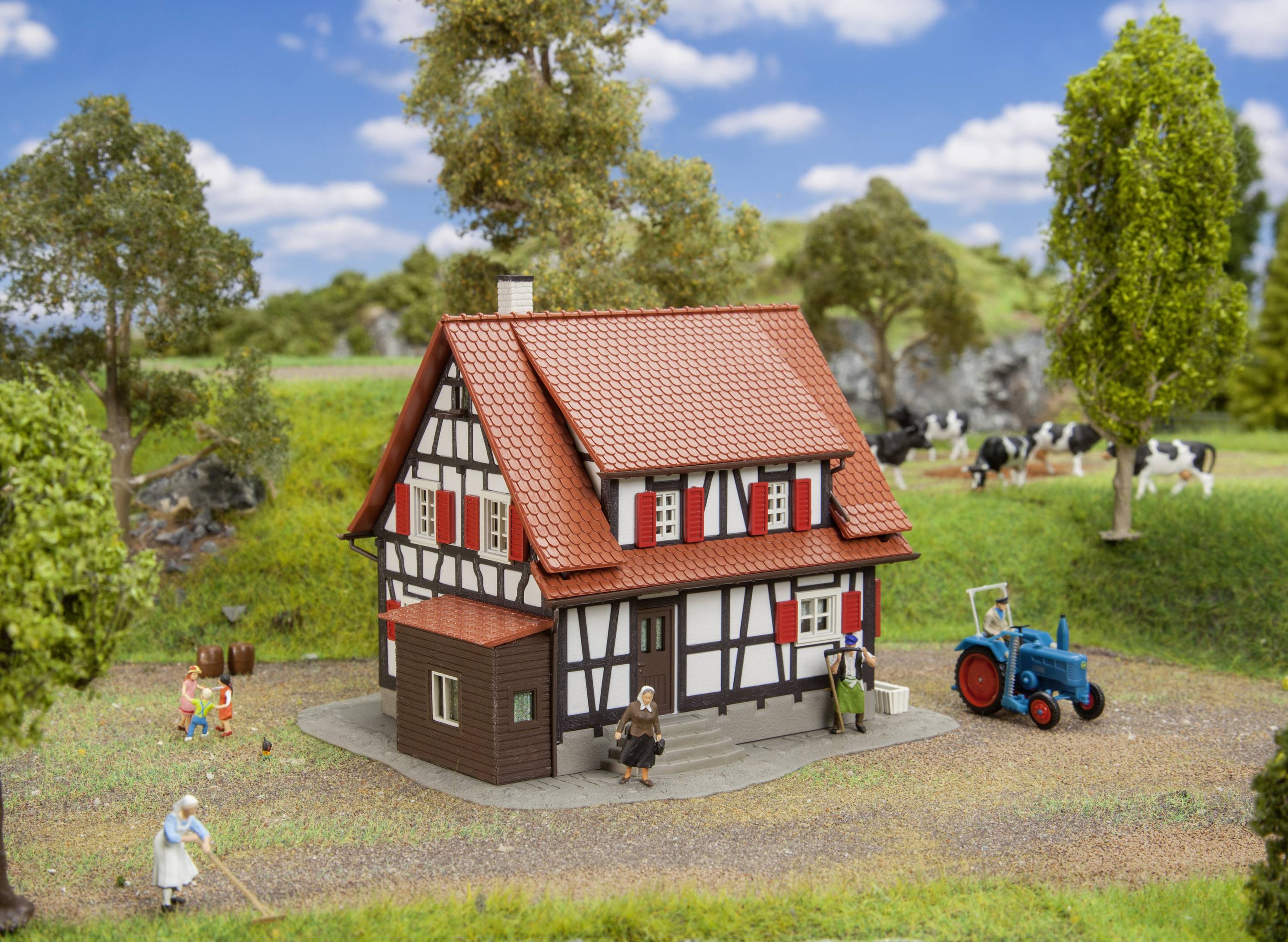 Een vakwerkhuis in een landelijke omgeving met bomen en weiland. Op de voorgrond een blauwe tractor en figuren die tuinwerkzaamheden verrichten.