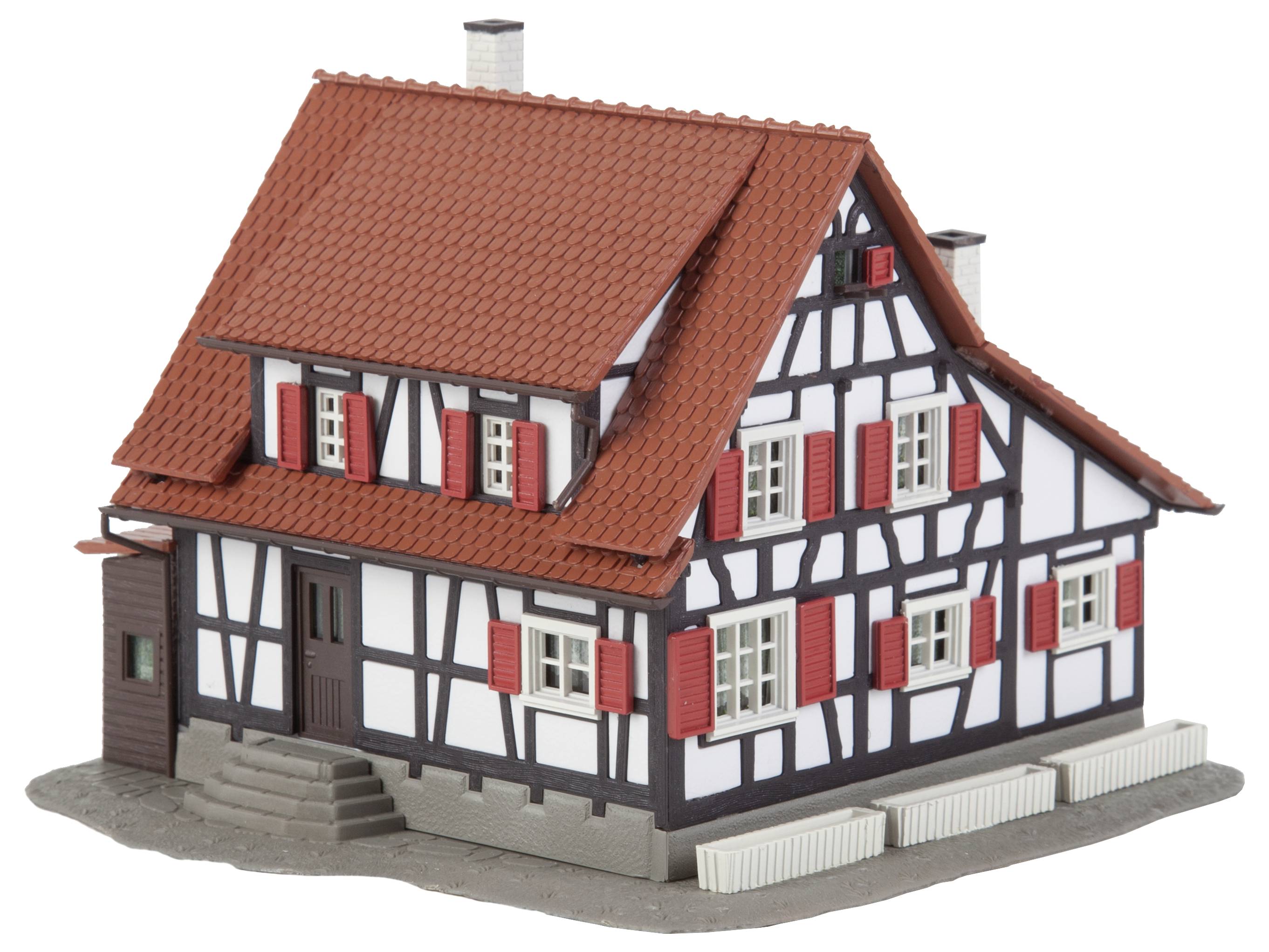 Vakwerkhuismodel met een rood pannendak, witte gevel en rode luiken, geplaatst op een grijze ondergrond.