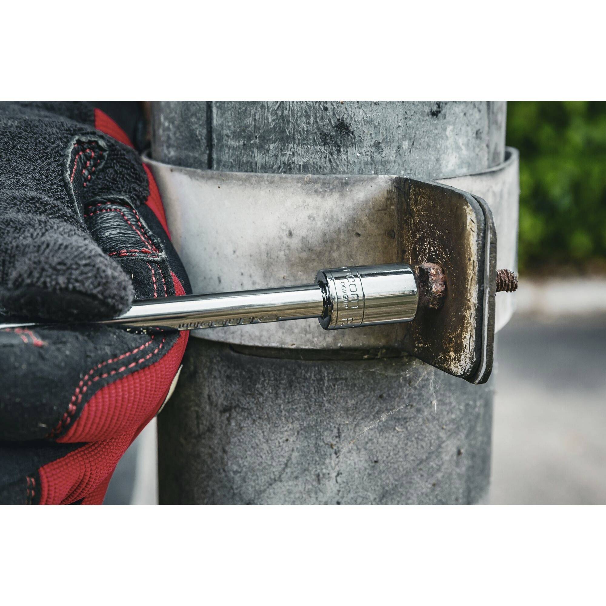 Een persoon met rode handschoenen draait een schroef vast aan een metalen buis met behulp van een moersleutel.