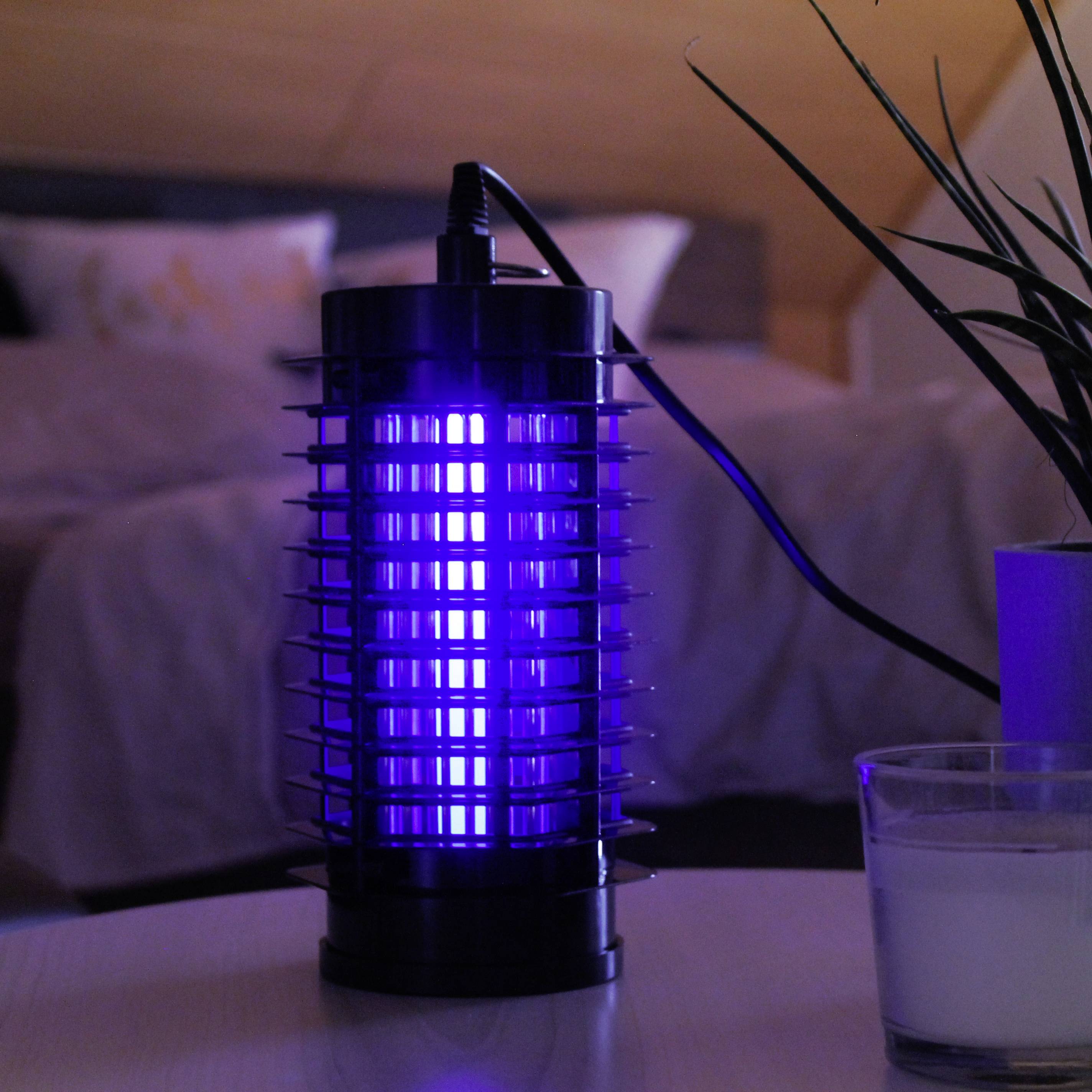 Blauw oplichtende insectenverdelger op een nachtkastje naast een kaars in een slaapkamer, illustreert een rustige avondsfeer.