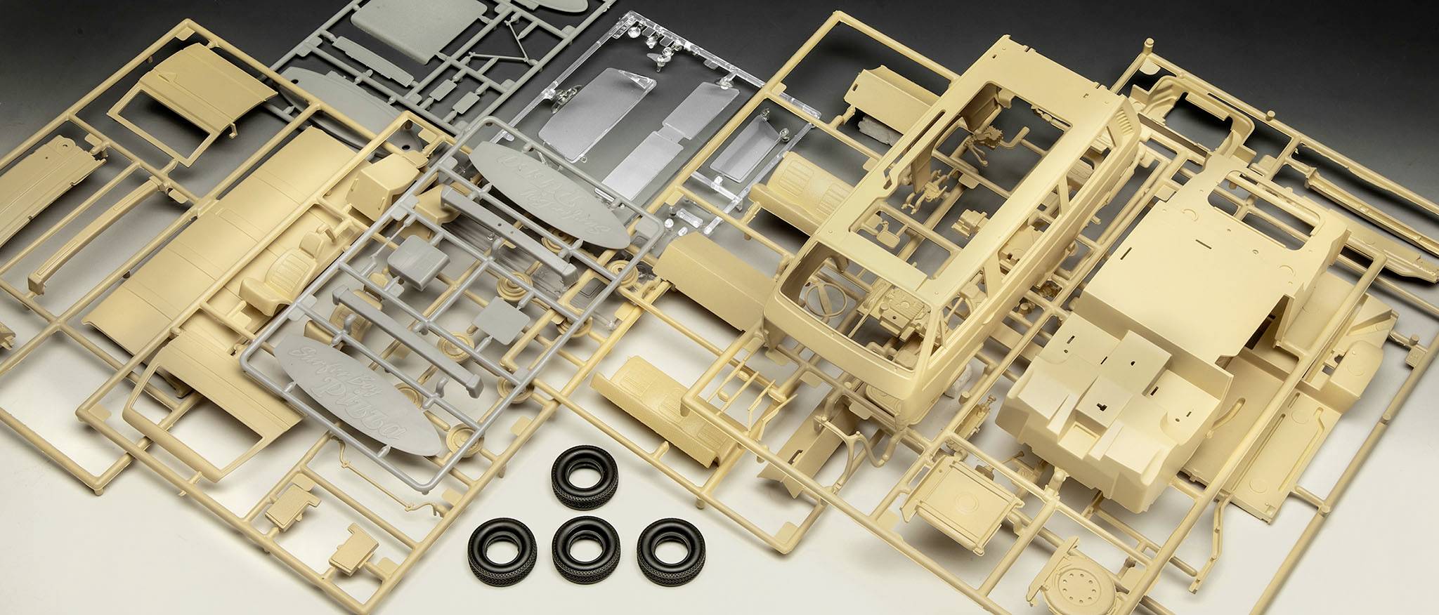 Verschillende ongemonteerde plastic modelbouwonderdelen in beige en grijs met vier zwarte banden, verspreid op een tafel.
